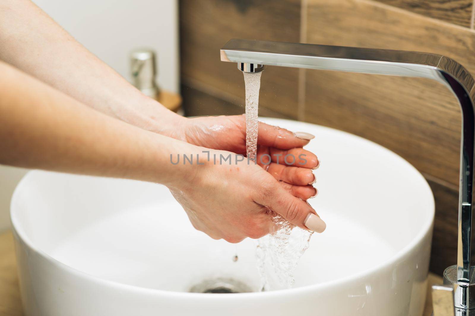 Hands of woman wash their hands in a sink to wash the skin and water flows through the hands. Concept of health, cleaning and preventing germs and coronavirus from contacting hands.