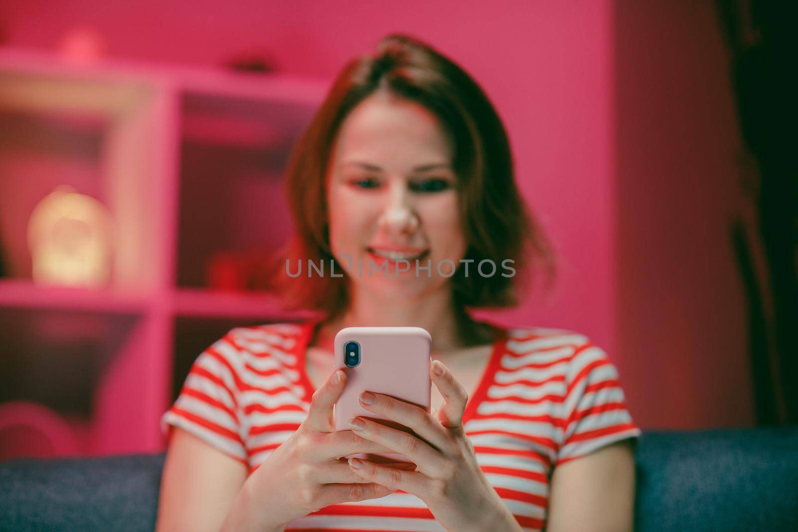 Young Woman Holding Smart Phone Looking at Cellphone Screen Laughing Enjoying Using Mobile Apps for Shopping. Having Fun Playing Games Chatting in Social Media Sit on Couch at Home by uflypro