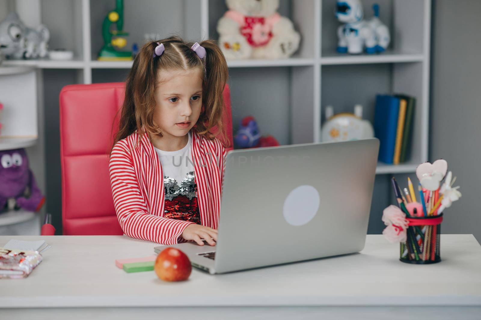 Pretty girl distance learning at home. Focused cute kid listening audio lesson studying at table, doing homework. Children remote education on quarantine concept by uflypro
