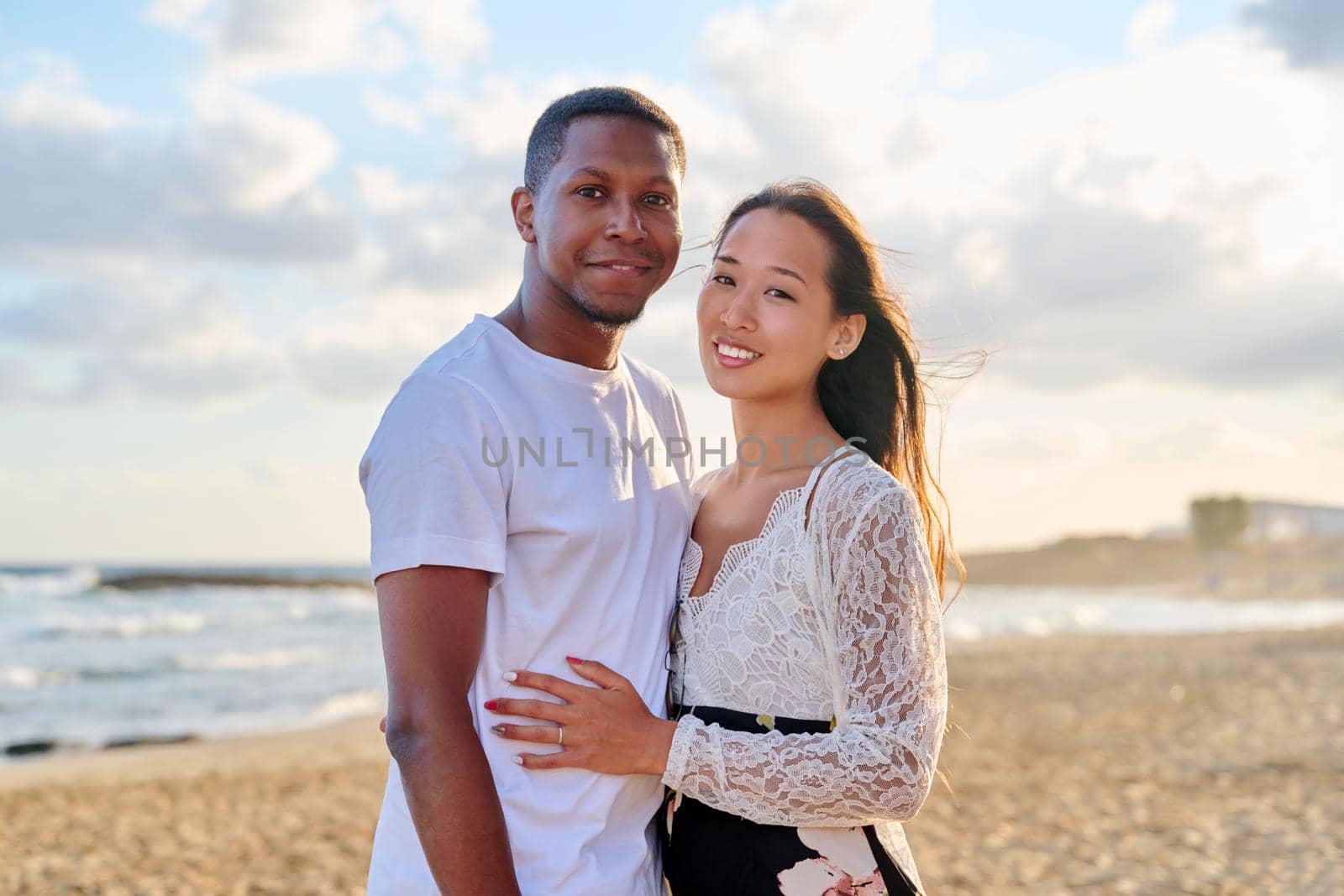 Loving romantic hugging young multiethnic couple on seashore. Happy african man and asian woman together. Love, relationship, dating, happiness, multicultural family, tourism, travel, people concept