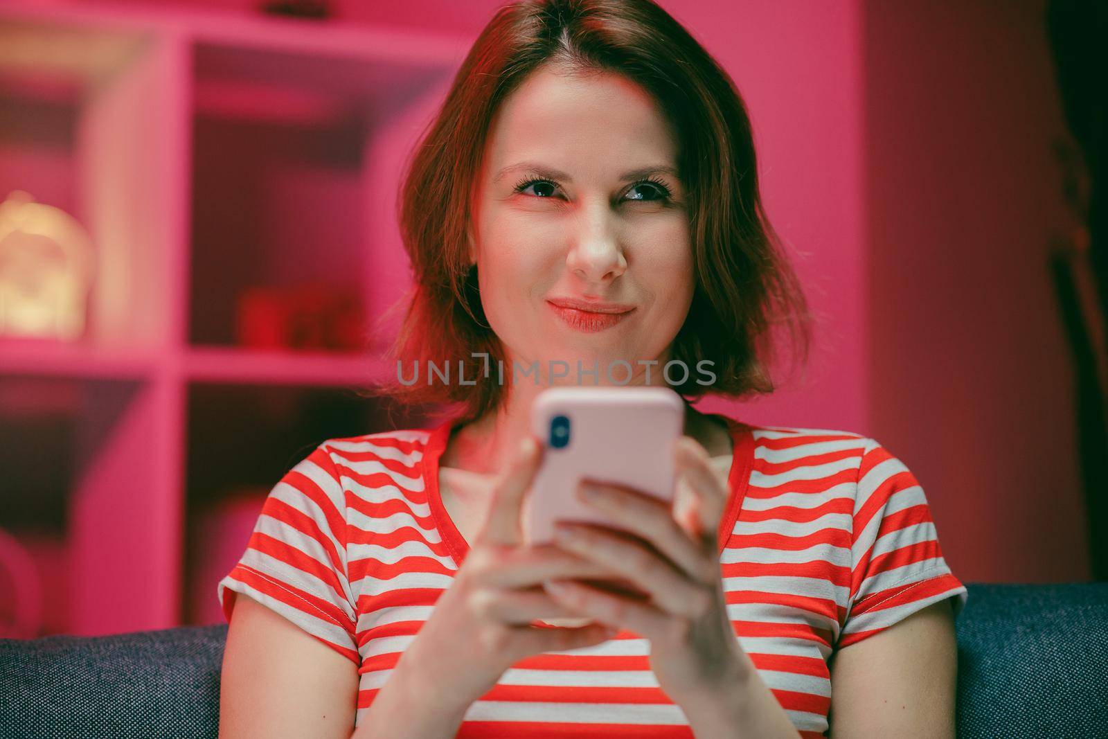 Happy Young Woman Holding Smart Phone Looking at Cellphone Screen Laughing Enjoying Using Mobile Apps for Shopping. Having Fun Playing Games Chatting in Social Media Sit on Couch at Home