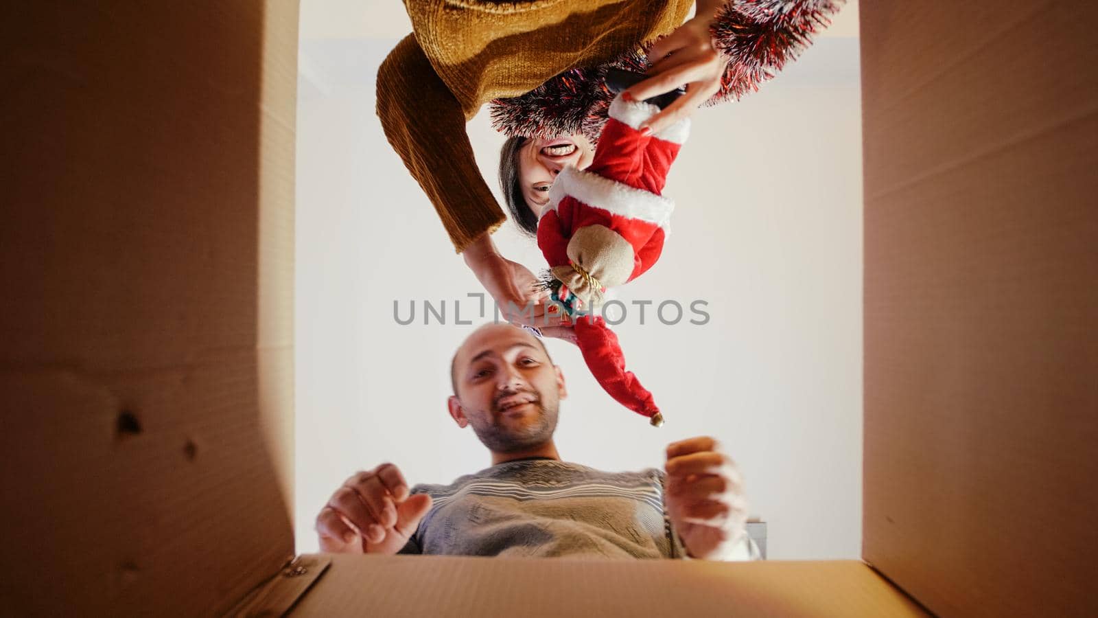 POV of man and woman opening box with garlands and ornaments, decorating for christmas eve. Festive couple feeling cheerful taking out decorations for holiday celebration and festivity