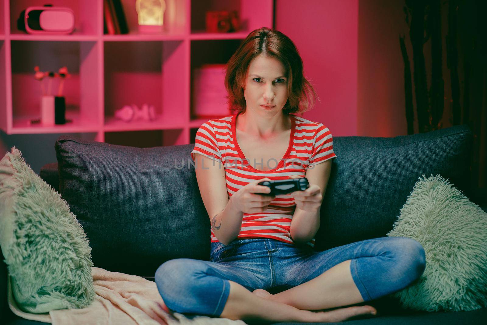 Woman play video games with wireless controller sitting on sofa. Playing in Video Games on a Console. She Plays with a Wireless Controller. Cozy Room is Lit with Warm and Neon Light.