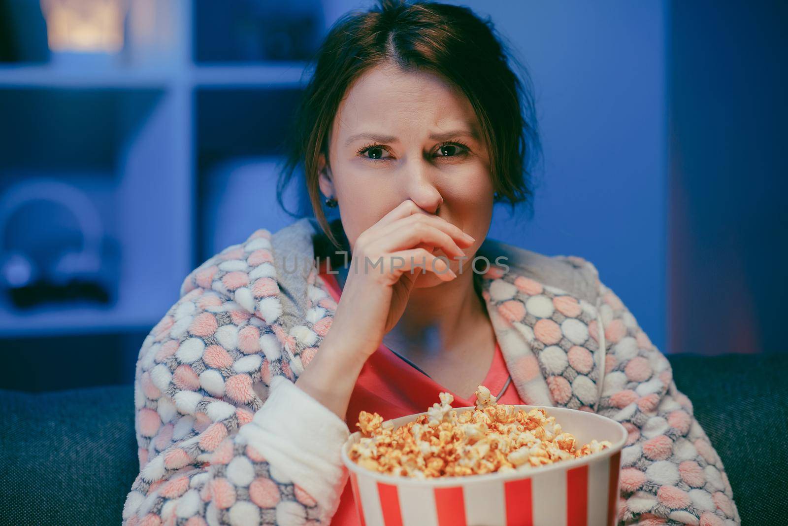 Young woman cry while watching a very moving movie with popcorn at night by uflypro