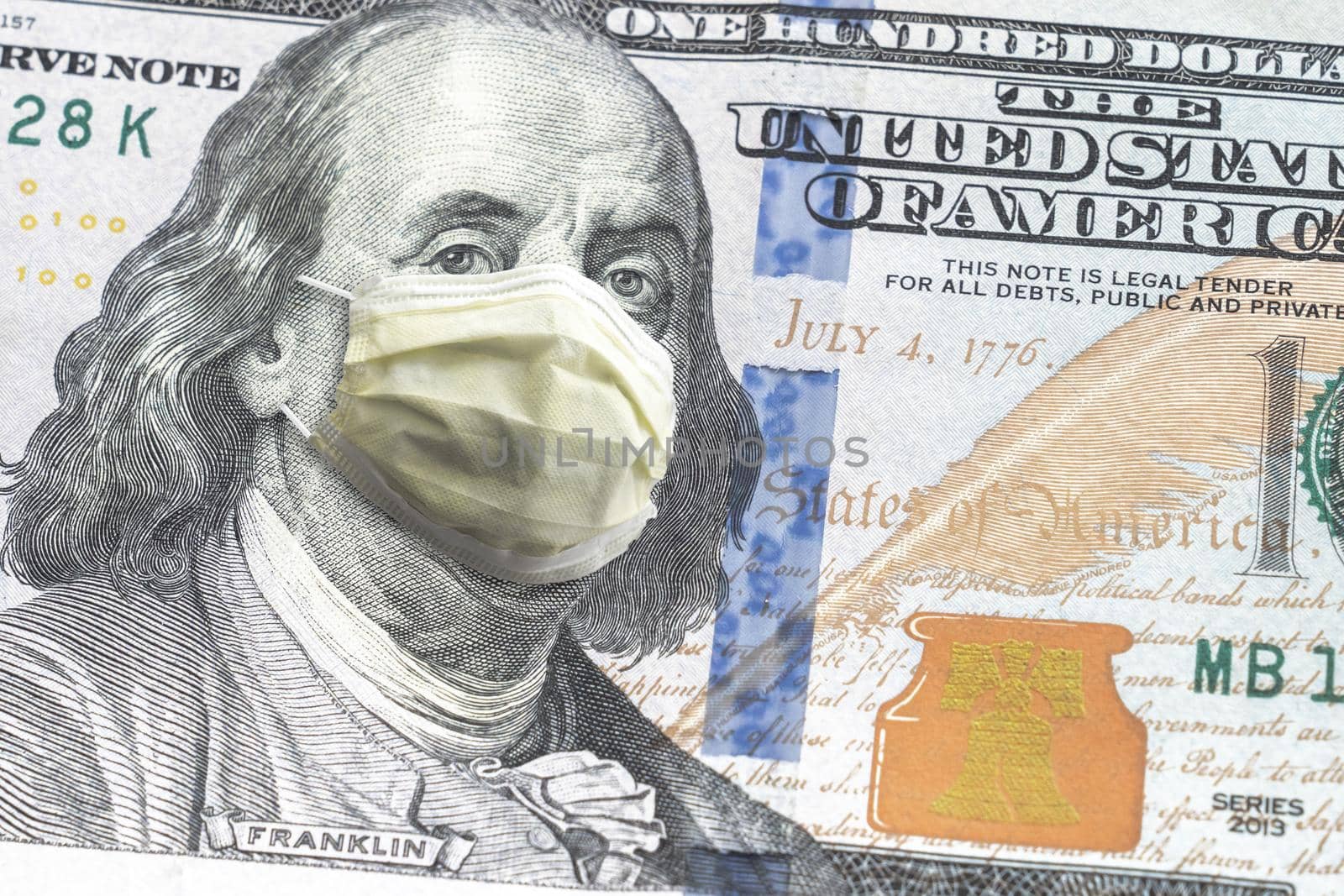 Close up of United States paper currency one hundred dollar bill with Benjamin Franklin wearing yellow doctor mask due to COVID-19 pandemic making a great finance or economic background amidst crisis.