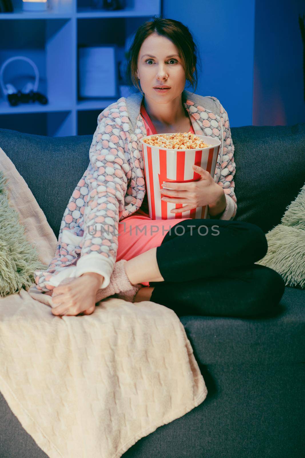 Beautiful girl face watching comedy film in home. Millennial woman sitting on sofa and watching TV. Concept of entertainment. Positive emotions.