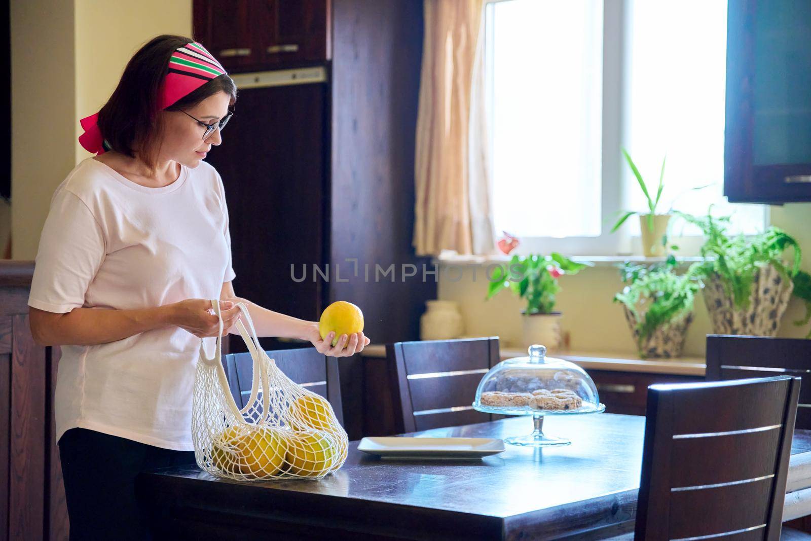 Woman at home kitchen with organic farm oranges in an eco-friendly mesh bag. Organic food fruit from eco farm, reusable shopping bag use, environmental protection, no plastic, no waste