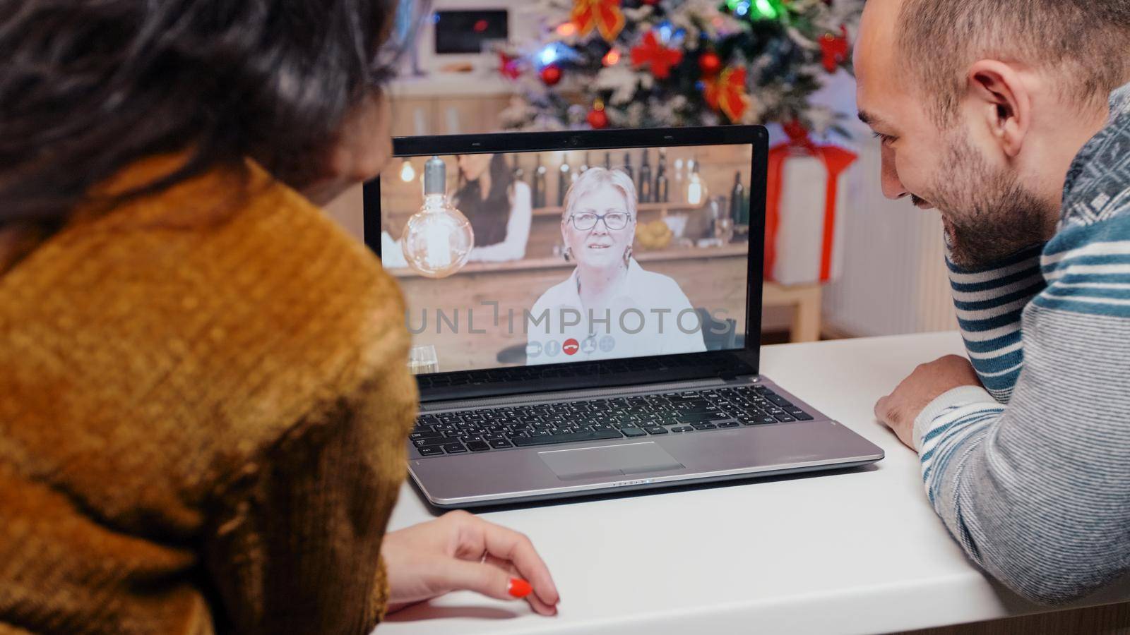 Couple talking to elder woman on video call for christmas celebration. Festive people using online conference for remote communication with senior adult on seasonal winter holiday.