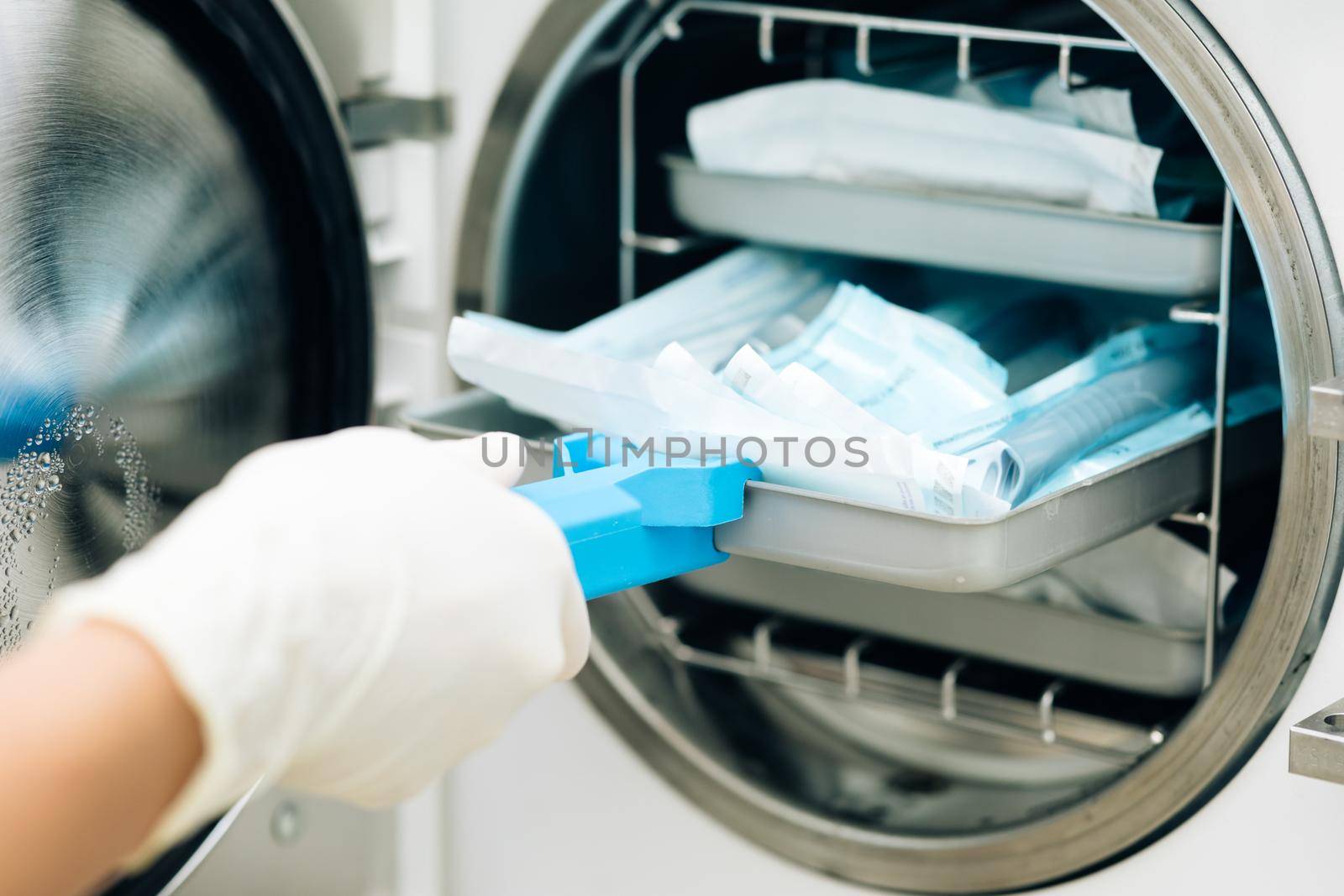 Tools sterilization, bacterial purification and disinfection in dental clinic. Nurse putting instruments in special craft paper bags into autoclave for processing. Modern laboratory equipment.