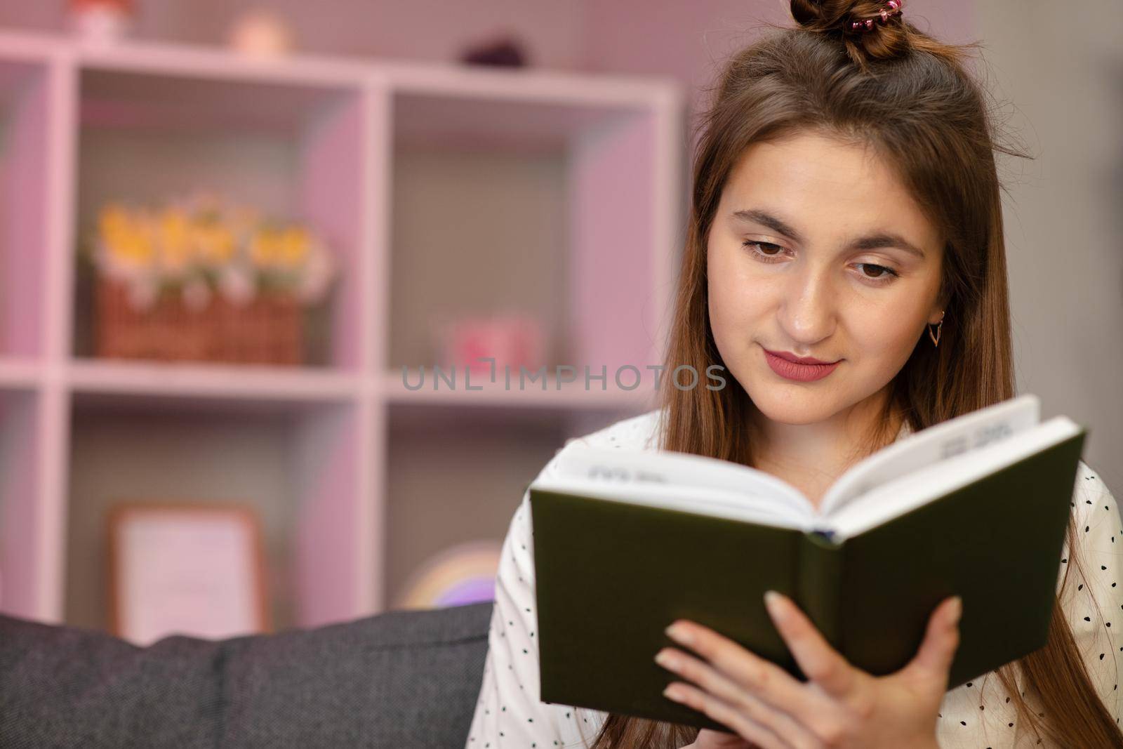 Portrait of a young student reading a book. Beautiful young brunette woman reading a book on the bed at home.