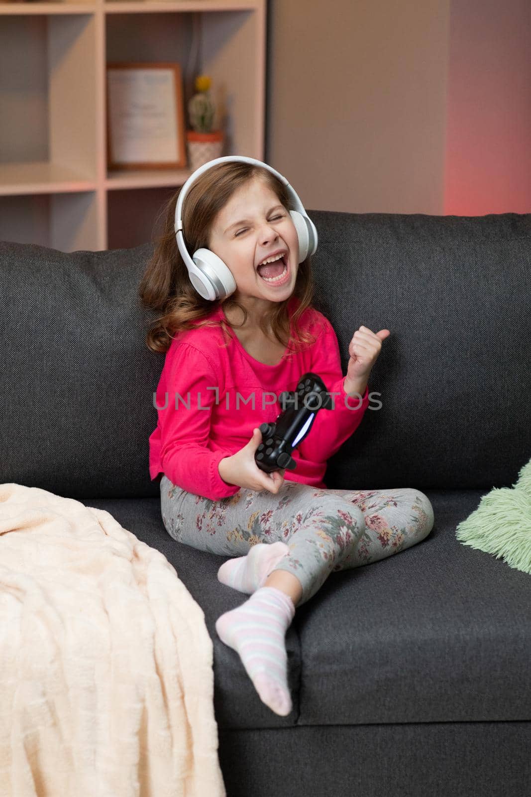 Little girl sitting on sofa playing a video in living room at home. Excited gamer girl hand holding joystick playing console game using a wireless controller. Having fun,enjoy happy expression.