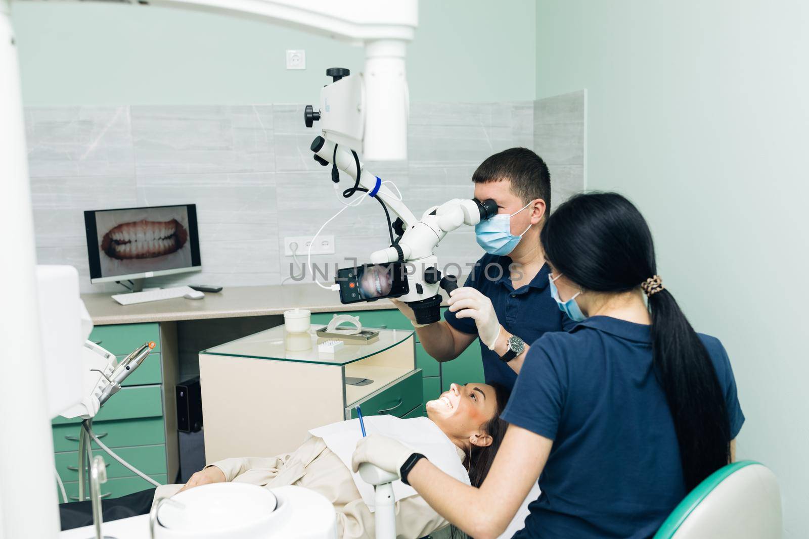 Dentist in latex gloves examining patient teeth in clinic. Patient lying with his open mouth in dentists office. Stomatologist performing examination using a microscope.