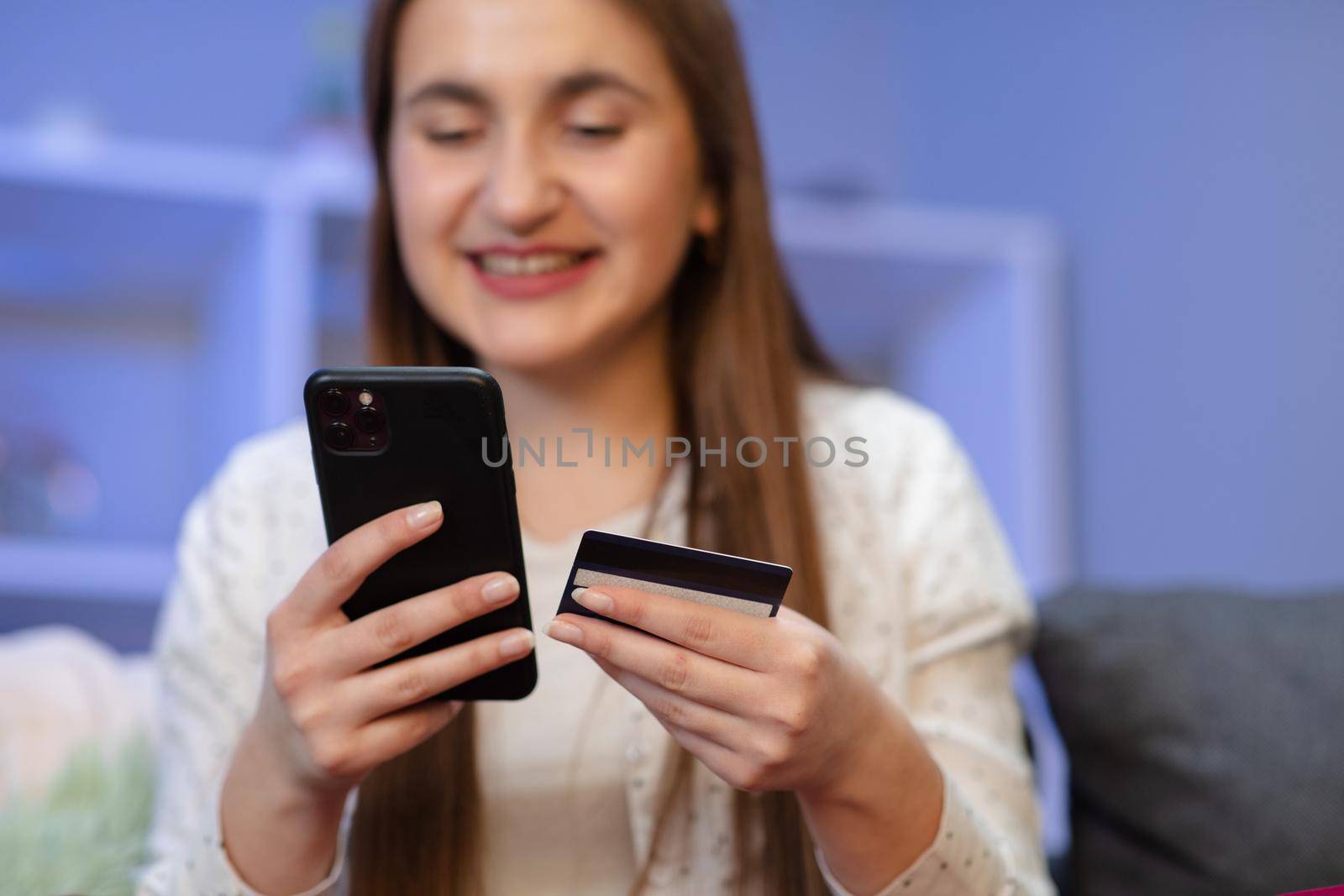 Young woman are buying online with a credit card while sitting on the sofa in the living room. Woman are using smartphone and doing online transactions by uflypro