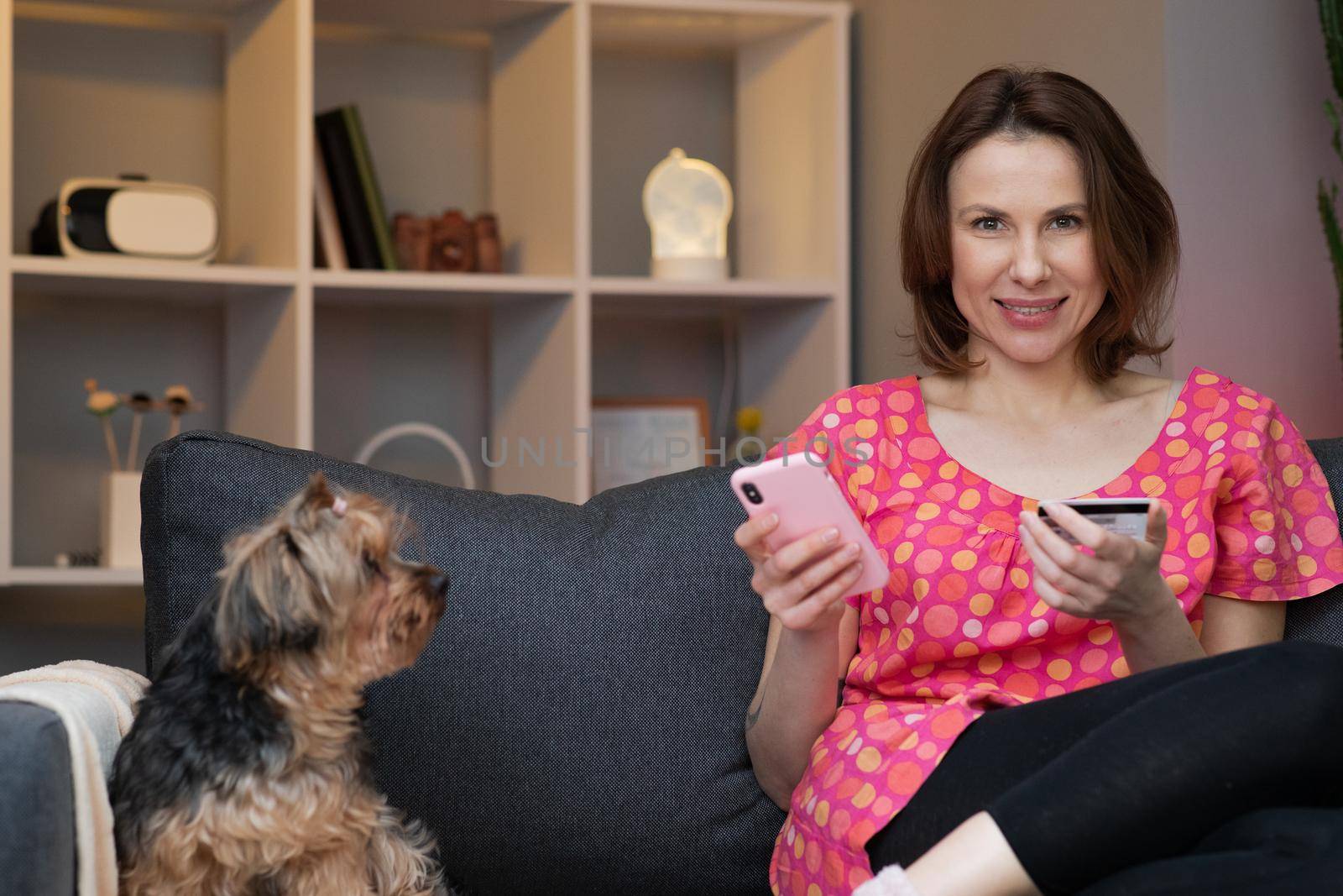 Woman are buying online with a credit card while sitting on the sofa in the living room. Women are using smartphone and doing online transactions. by uflypro