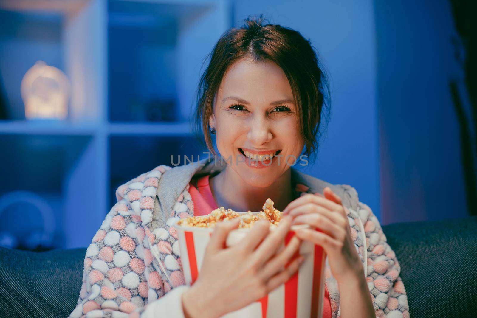 Portrait shot of the cheerful young Caucasian beautiful woman watching comedy film eating popcorn