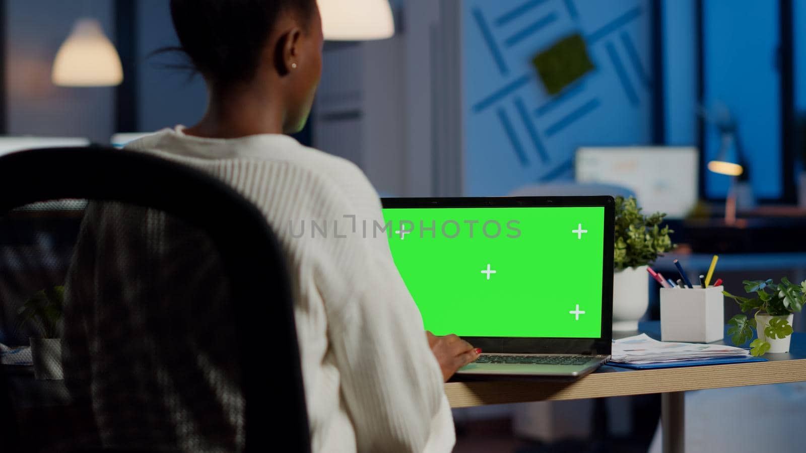 African businesswoman reading on laptop with greenscreen display, green mockup, chroma key monitor sitting at desk in business office late at night. Freelancer watching at isolated desktop overwork