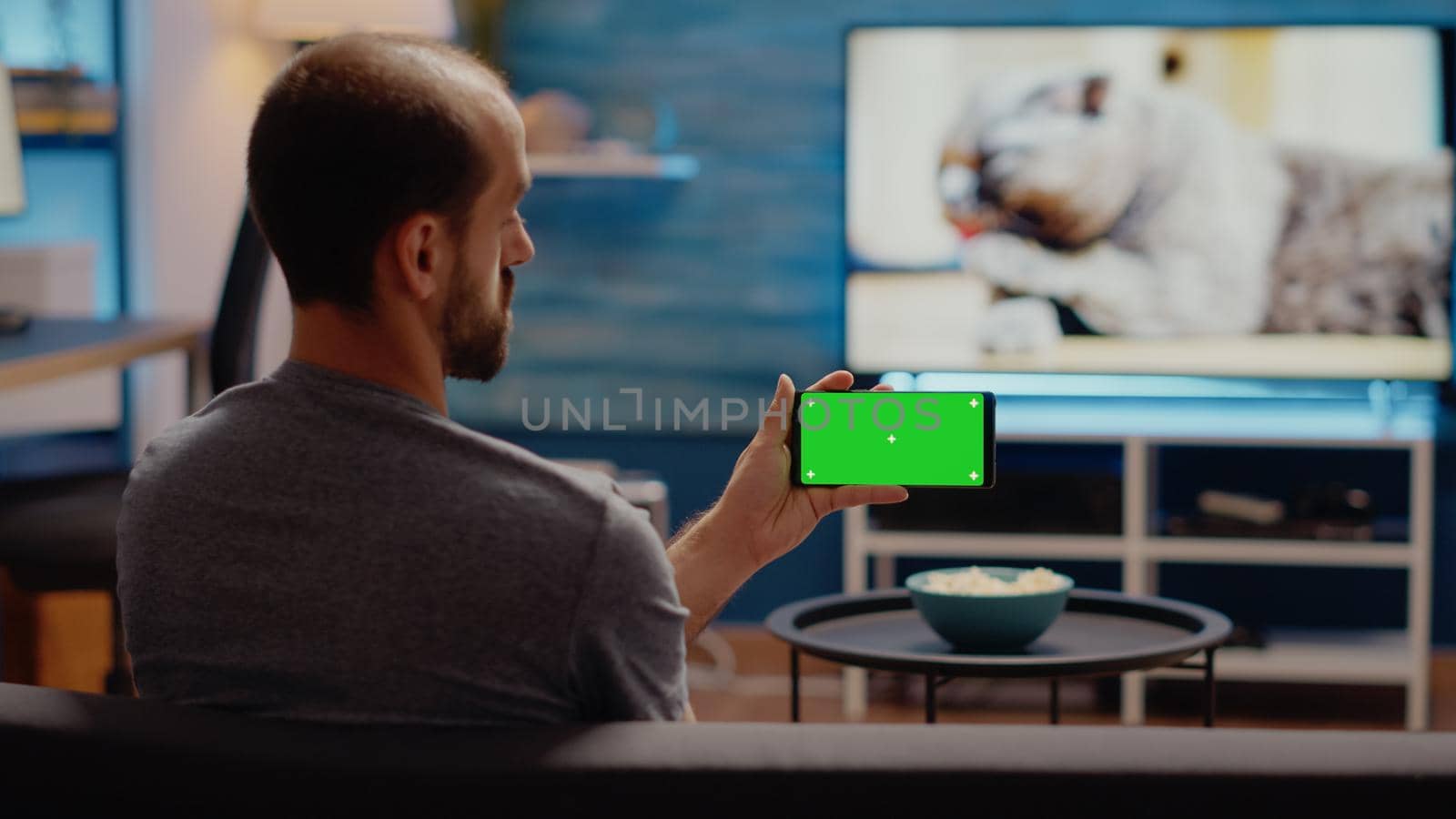 Young man watching horizontal green screen on smartphone by DCStudio
