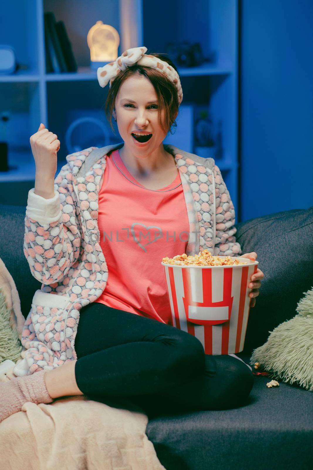 Happy beautiful girl face watching comedy film in home. Millennial woman sitting on sofa and watching TV. Concept of entertainment. Positive emotions by uflypro
