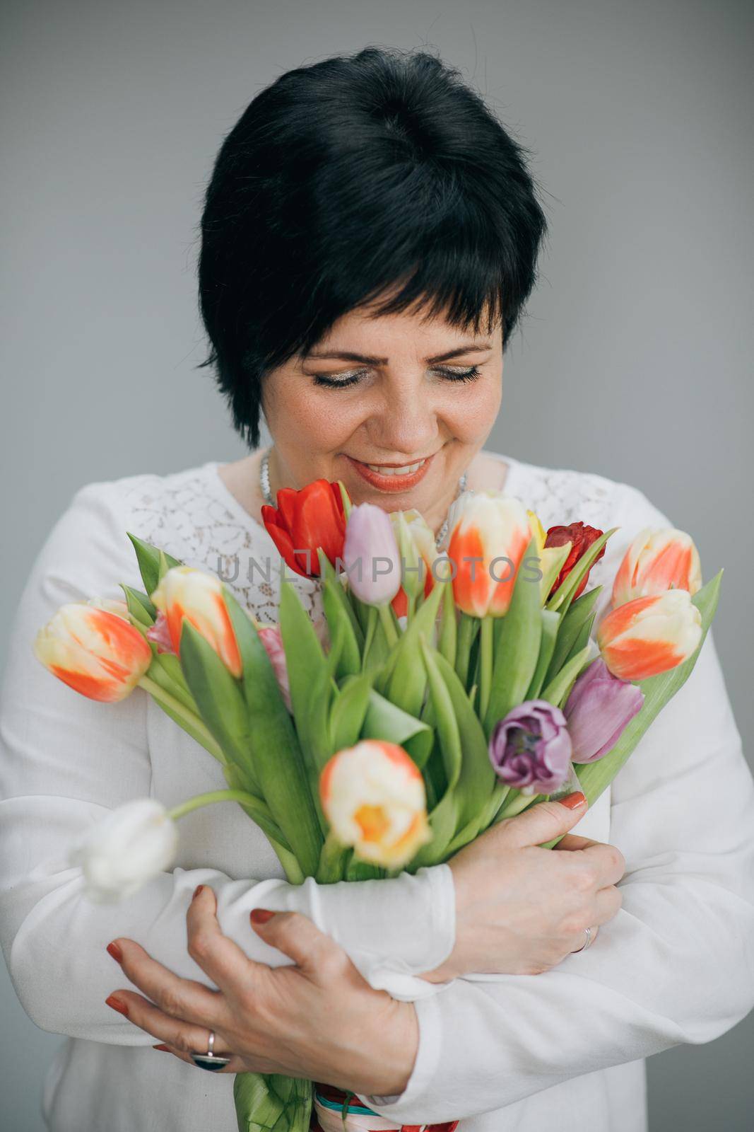 Woman holding in her hands freshly flower bouquet on the grey wall background.
