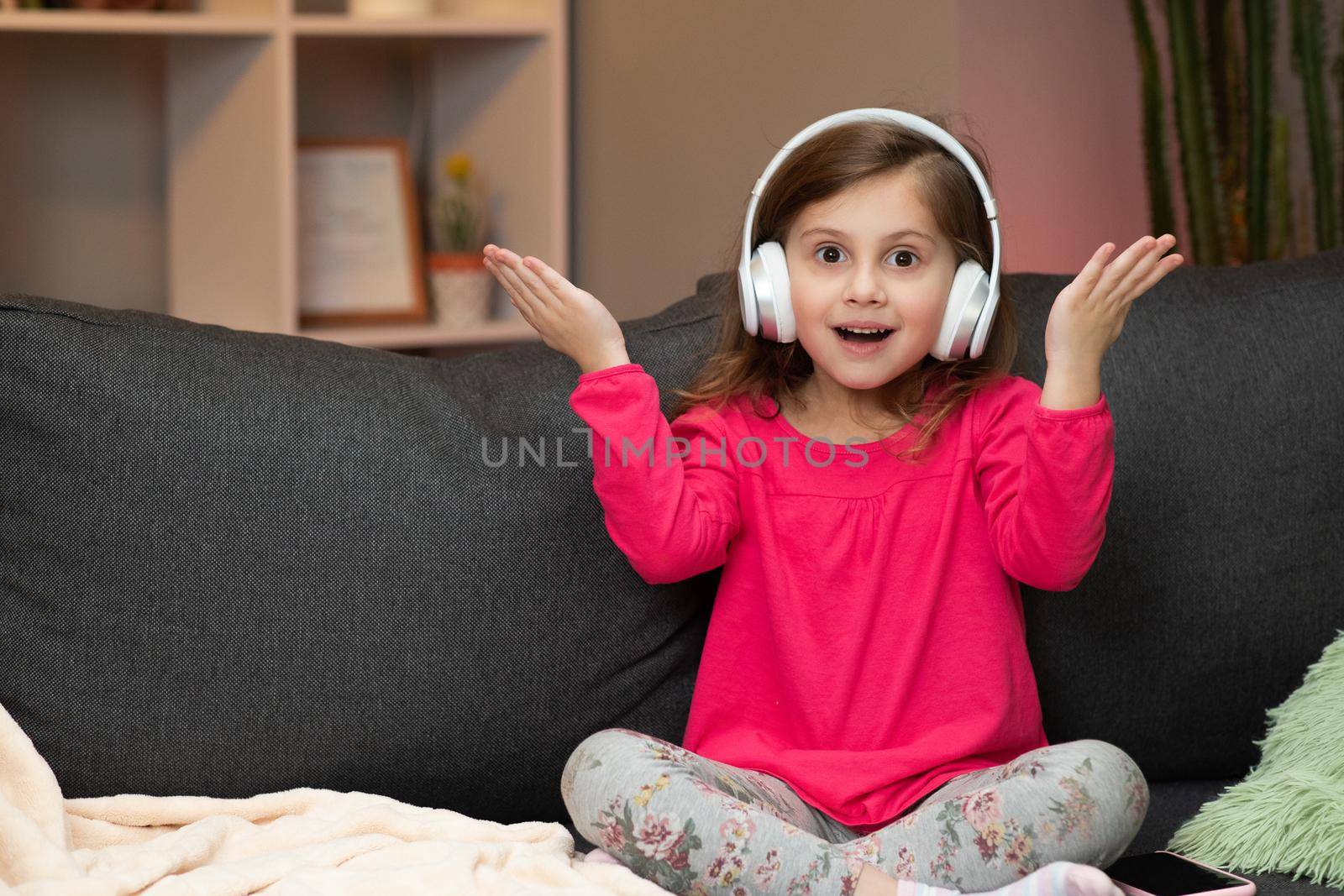 Little Girl Listens To Music On Wireless Headphones. Funny Little Girl Dancing, Singing And Moving To Rhythm. Kid Wearing Headphones. by uflypro