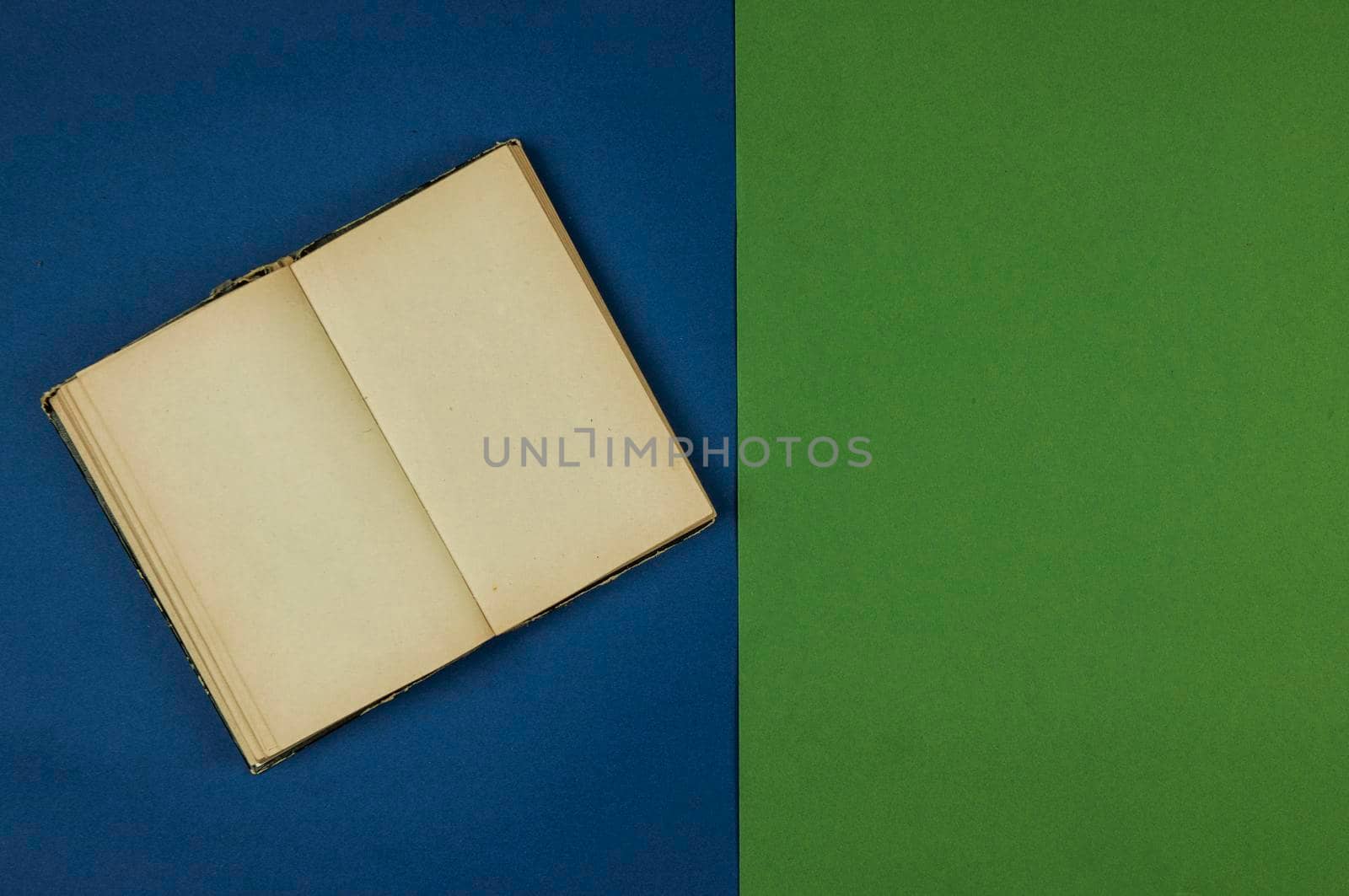 old open book with blank pages is lying on green and blue background. Copy space. Top view    