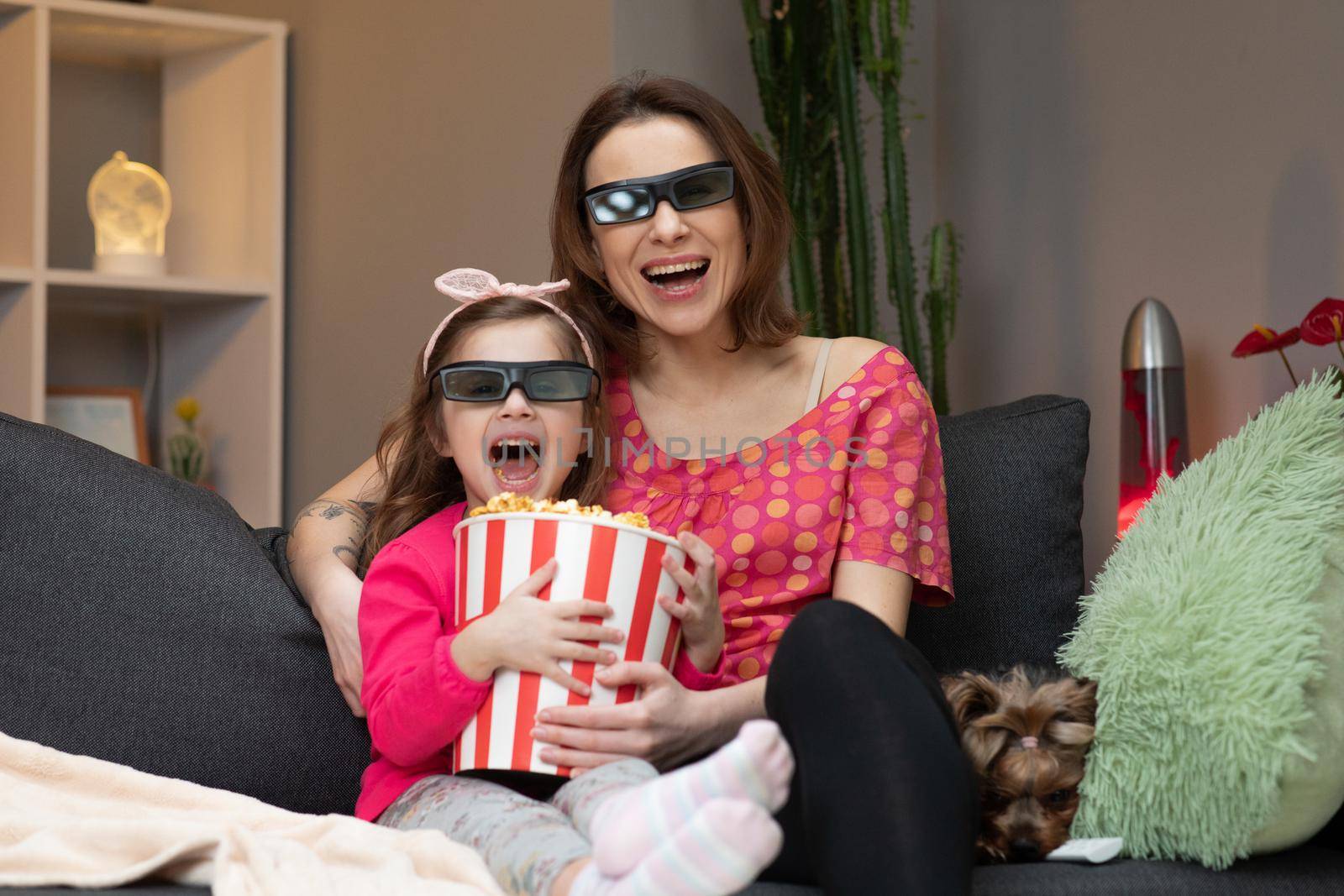 Woman with a little girl Wearing 3d Glasses watching tv and eating popcorn. Family time relax with young girl kid on sofa in living room concept