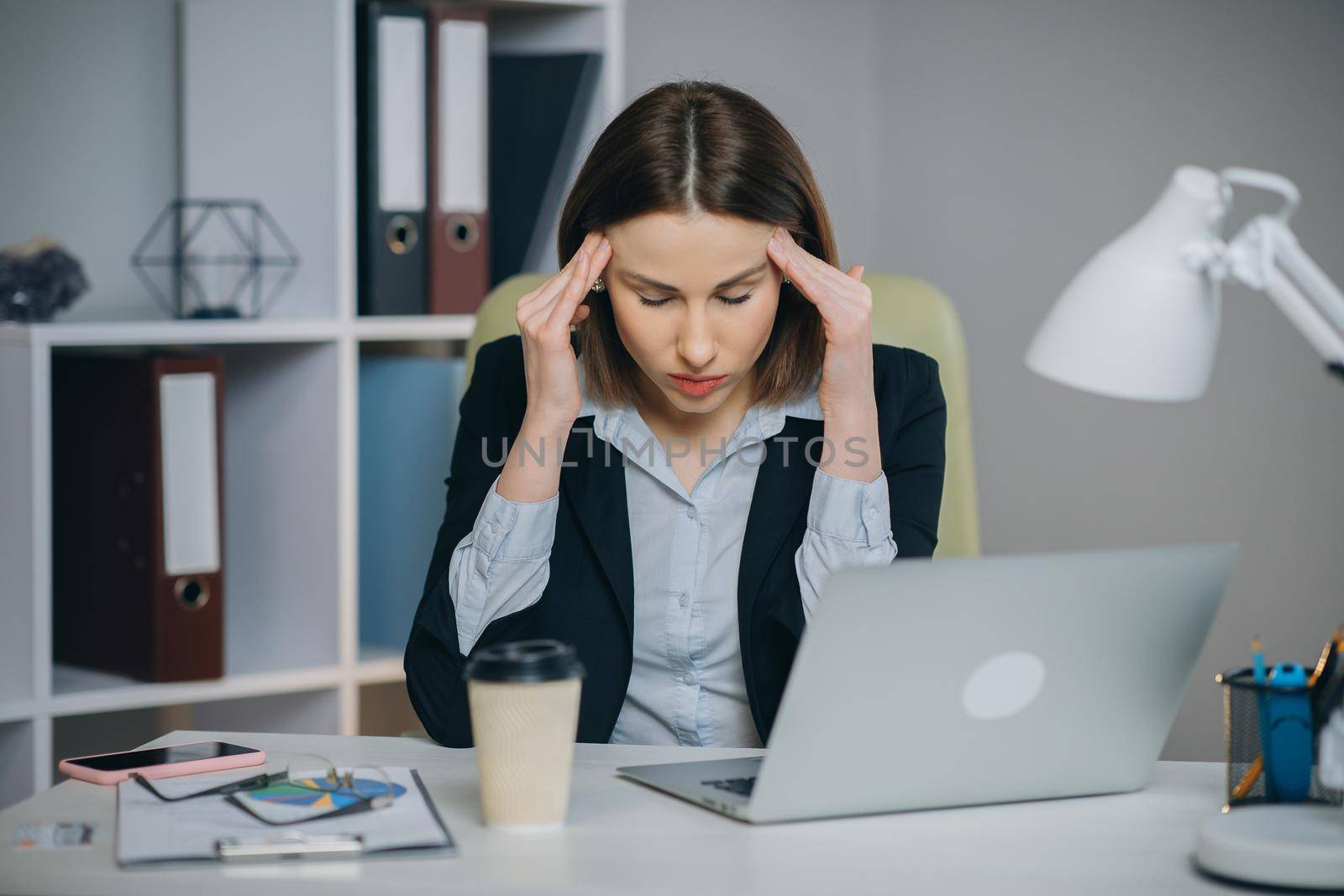 Feeling Tired and Stressed. Frustrated Young Woman Keeping Eyes Closed and Massaging Nose While Sitting at Her Working Place in Office. by uflypro