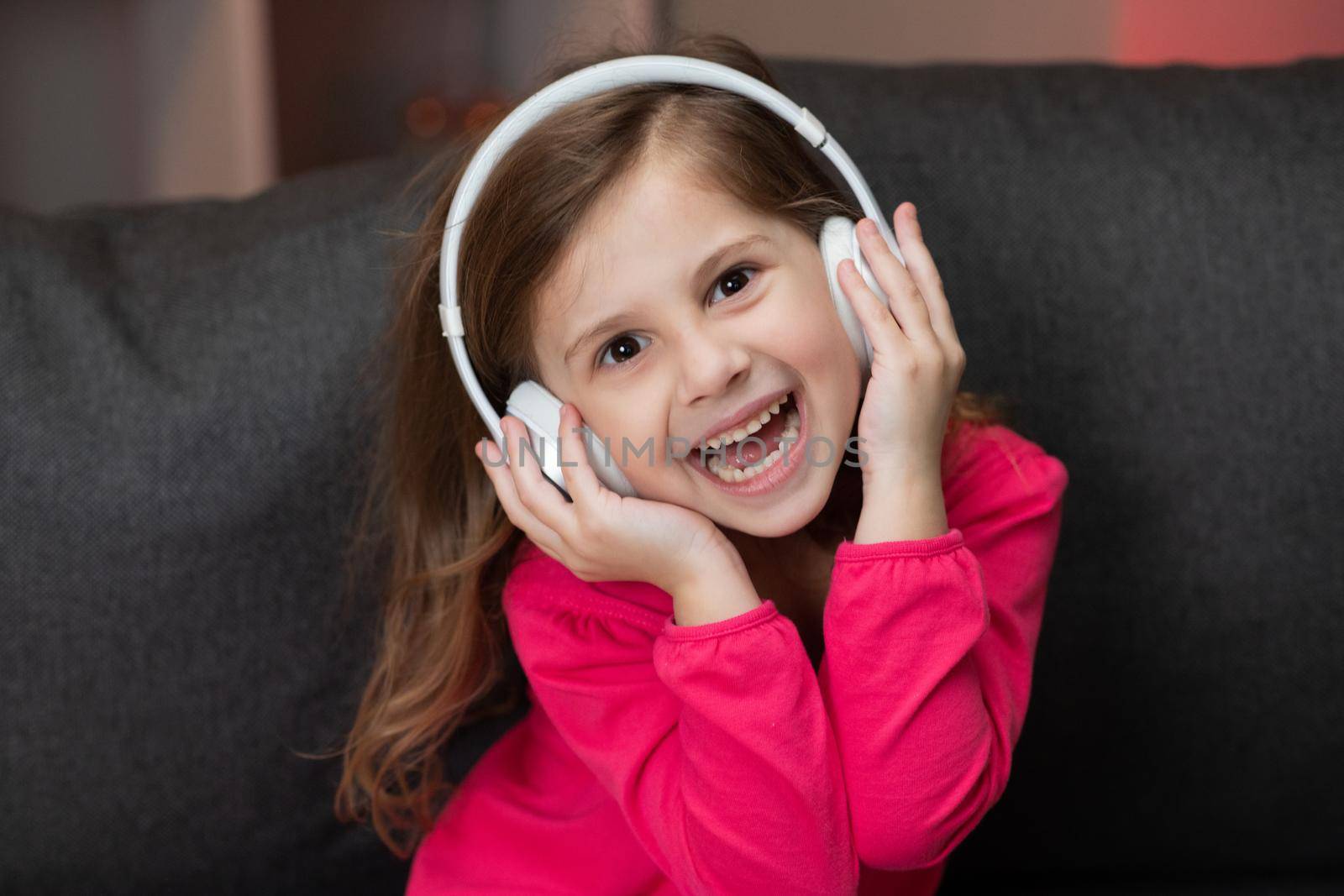 Cute Happy Little Girl Listens To Music On Wireless Headphones. Funny Little Girl Dancing, Singing And Moving To Rhythm. Kid Wearing Headphones.
