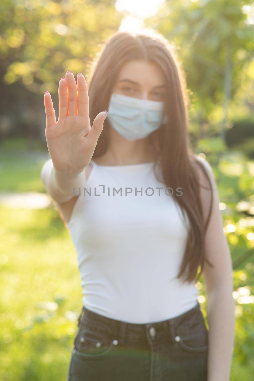 Portrait of a young woman wearing protective mask makes stop sign with hand, saying no, expressing restriction. Concept health and safety, N1H1 coronavirus quarantine, virus protection. by uflypro