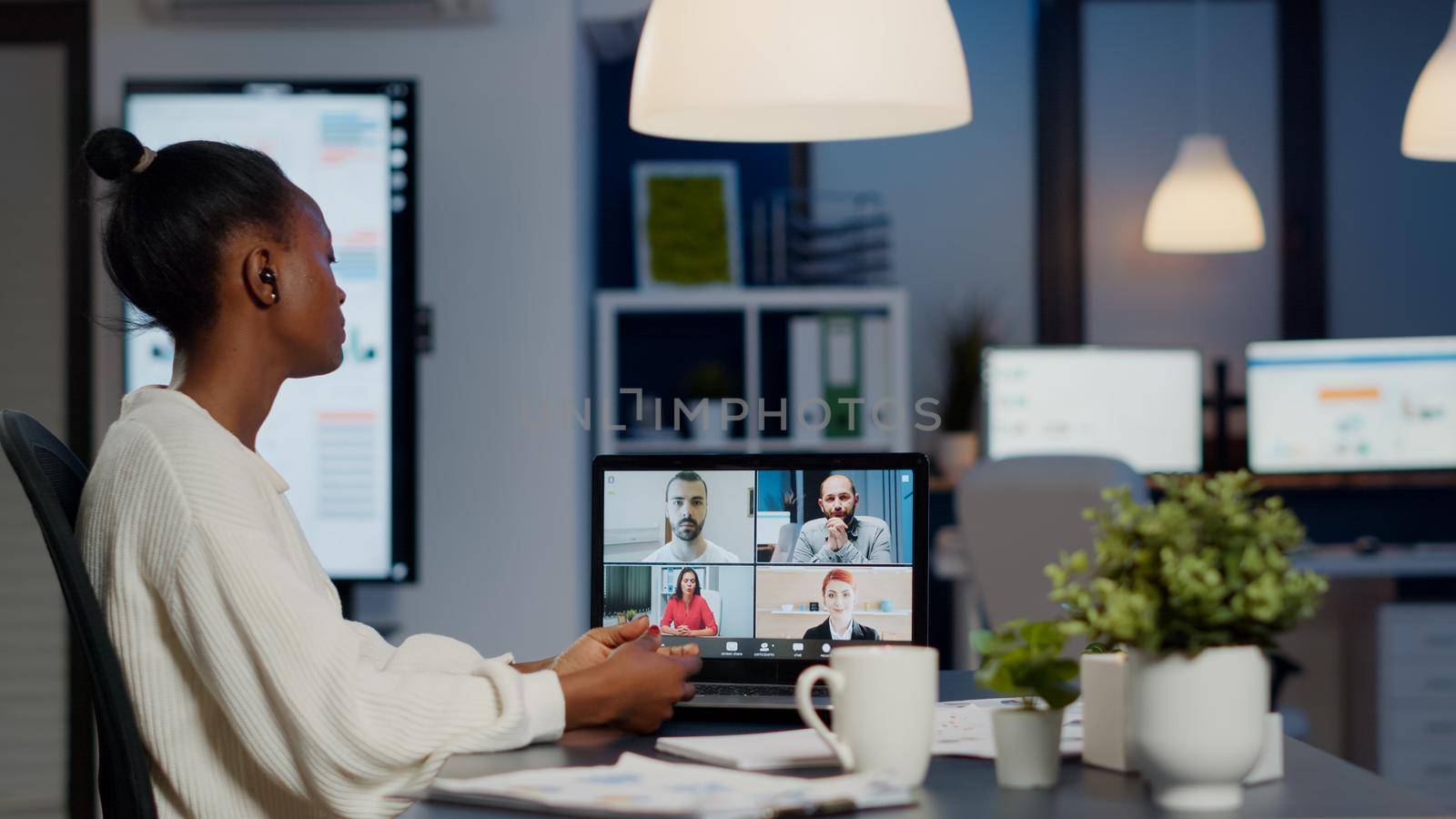 African businesswoman talking during video conference with team in midnight using laptop in start up business office. Diverse workers talking during corporate meeting using technology network wireless