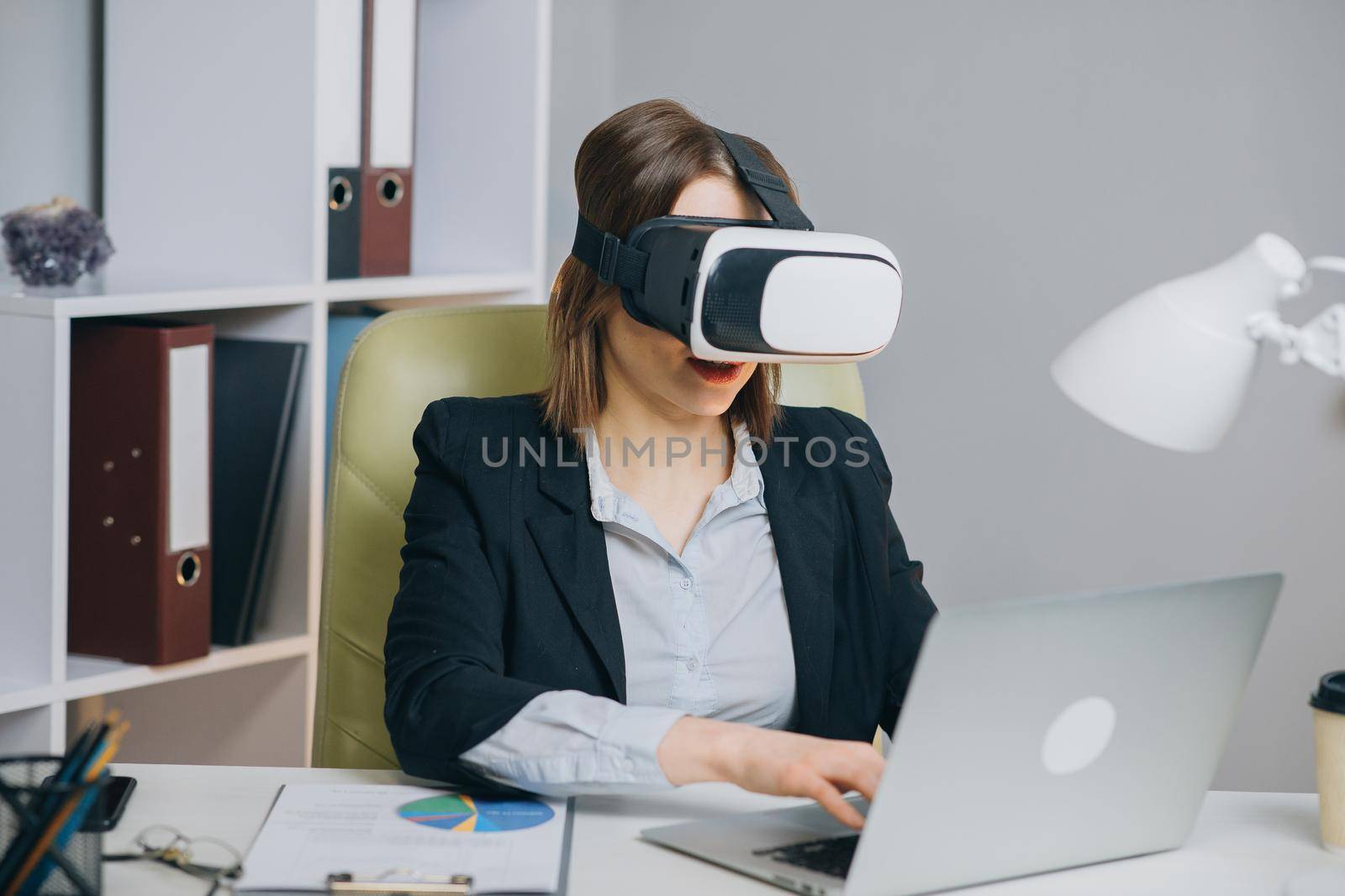 Woman wearing virtual reality glasses in office. Young girl using VR goggles in office. Pretty woman working in augmented reality at workplace. by uflypro