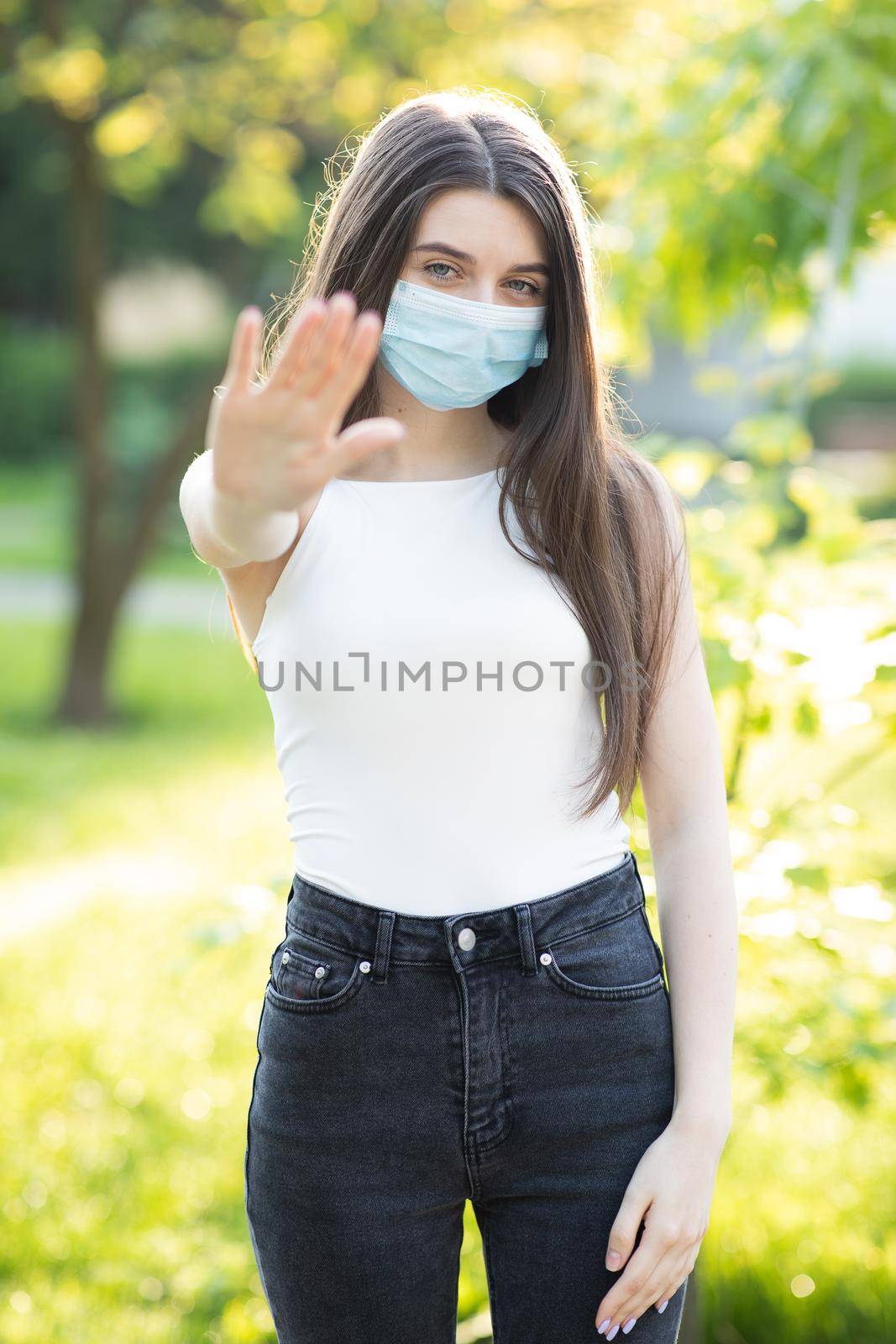 Portrait of a young woman wearing protective mask makes stop sign with hand, saying no, expressing restriction. Concept health and safety, N1H1 coronavirus quarantine, virus protection. by uflypro