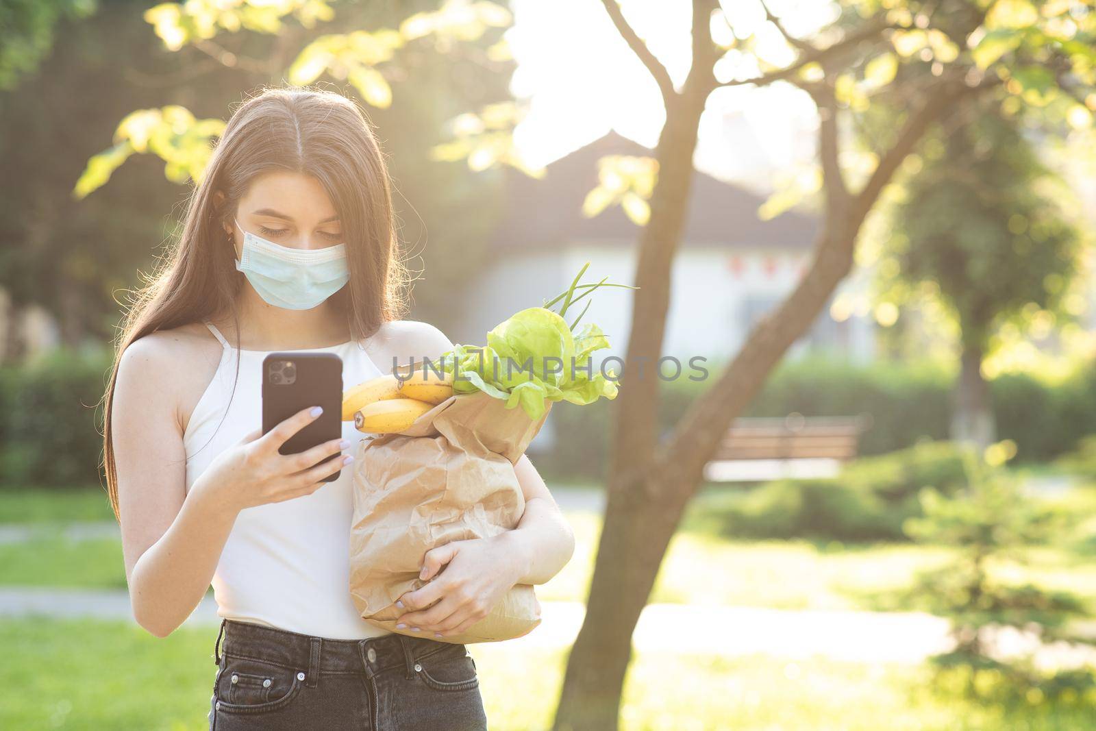 Social distancing. Food delivery. Woman wearing face masks in prevention of coronavirus during quarantine. Woman Using the Mobile Phone. Pandemic.