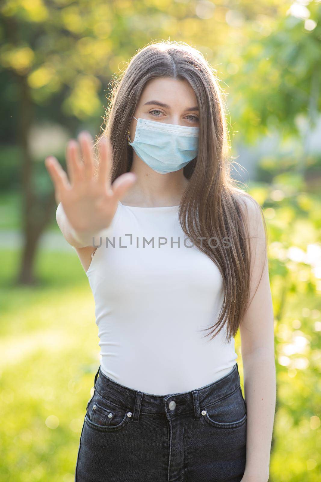 Vertical Portrait of a young woman wearing protective mask makes stop sign with hand, saying no, expressing restriction. Concept health and safety, N1H1 coronavirus quarantine, virus protection by uflypro