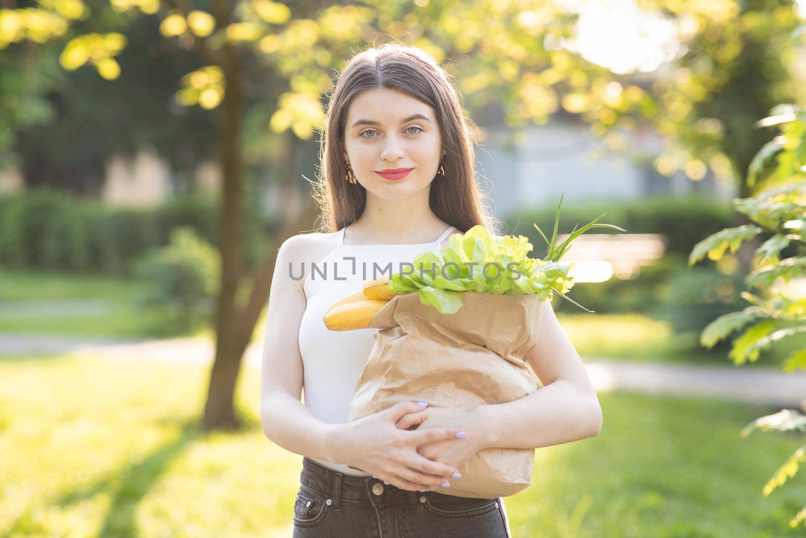 Happy young woman shopaholic holding paper shopping bags isolated on green background in the park. Concepts for sales and shopping.