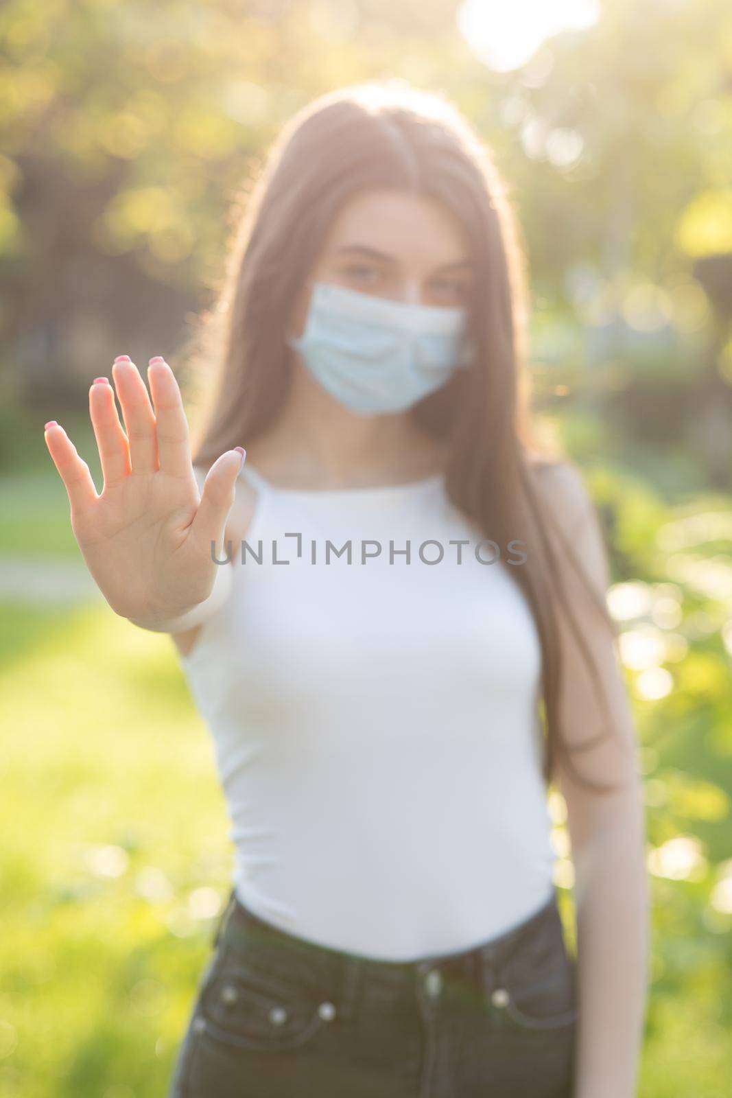 Young woman wearing protective mask makes stop sign with hand, saying no, expressing restriction. Concept health and safety, N1H1 coronavirus quarantine, virus protection. by uflypro