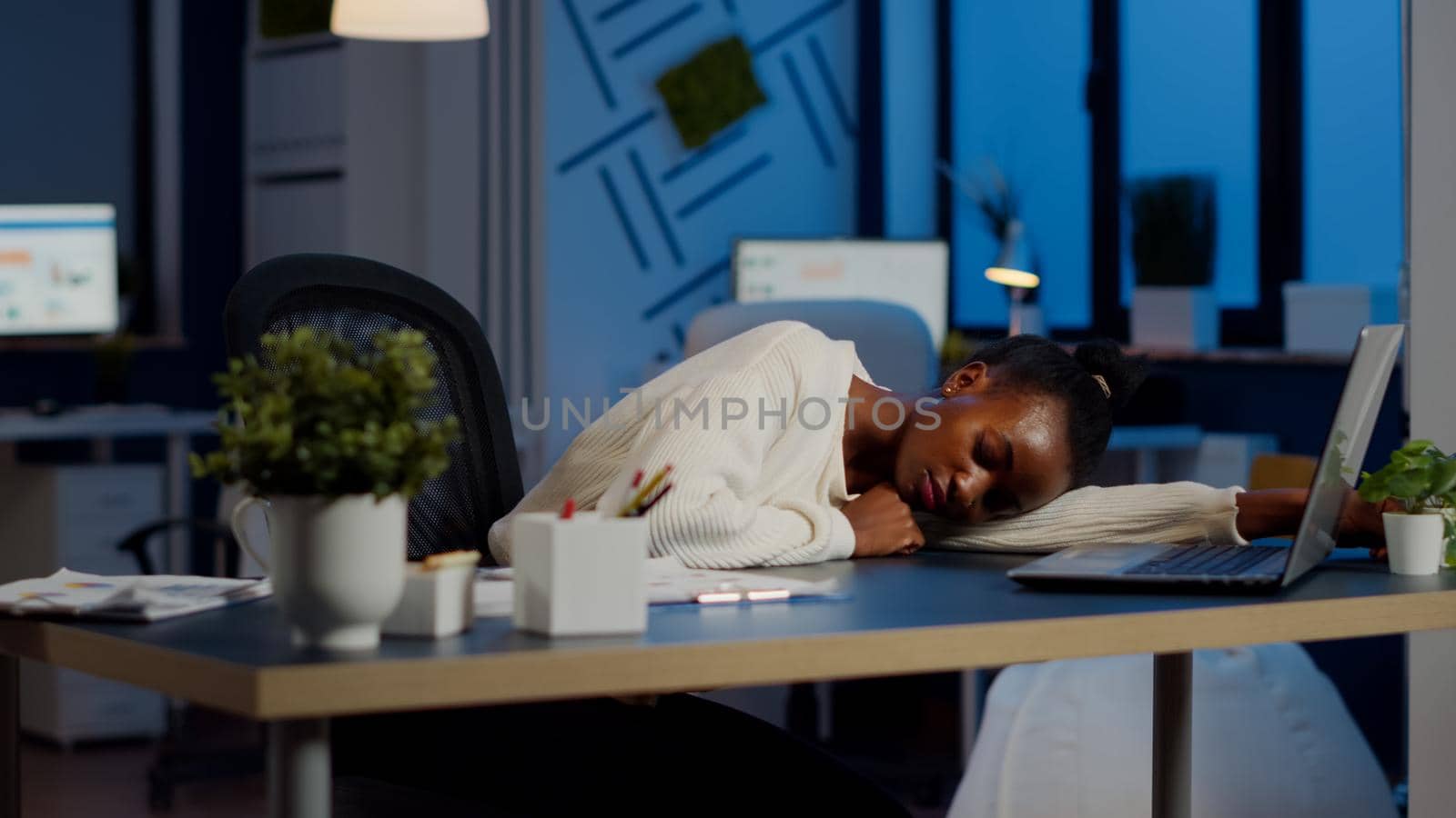 Exhausted overload african business woman falling asleep on desk with open laptop monitor while working in start up company. Overworked employee using doing overtime respecting deadline, sleeping