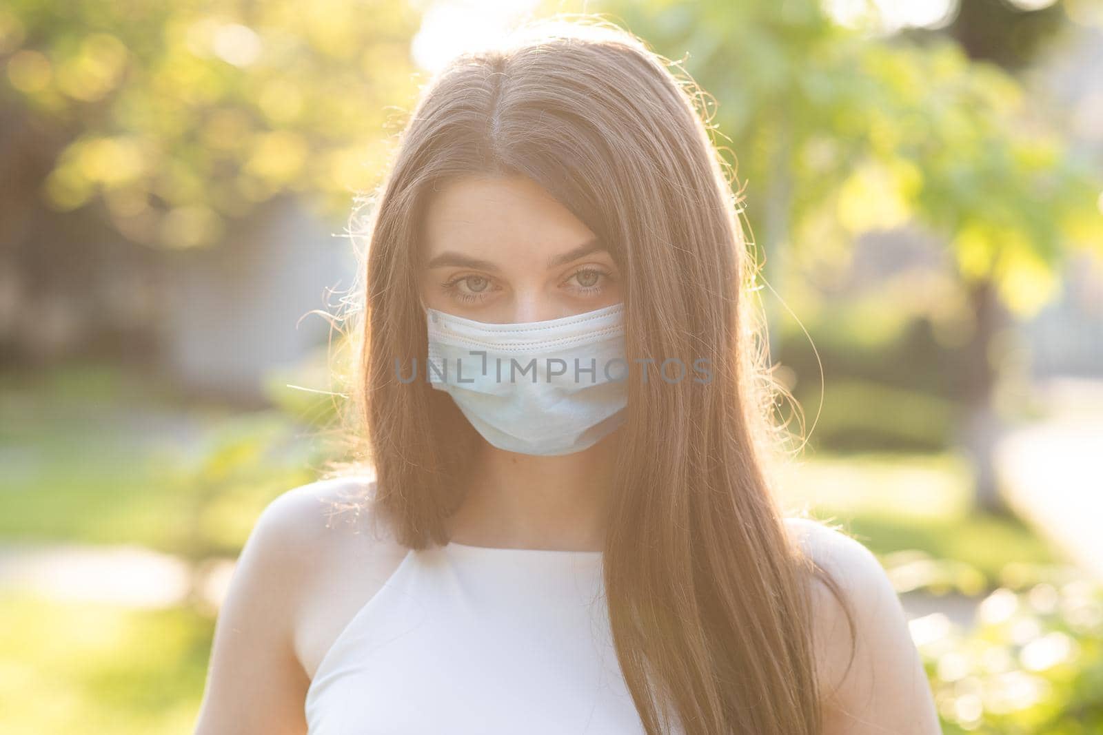 Close up portrait Young woman in medical mask. Female breathes deeply looking at camera. Isolated on park background. Health care and medical concept. by uflypro