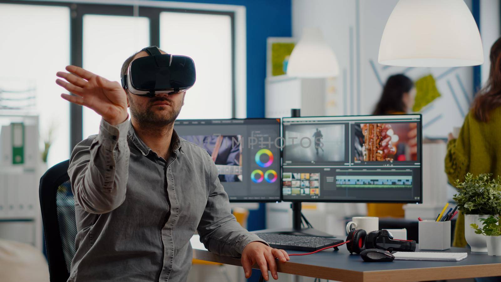 Video editor experiencing virtual reality headset, gesturing, editing film montage using post production software working in creative agency office. Videographer using VR goggles in multimedia company