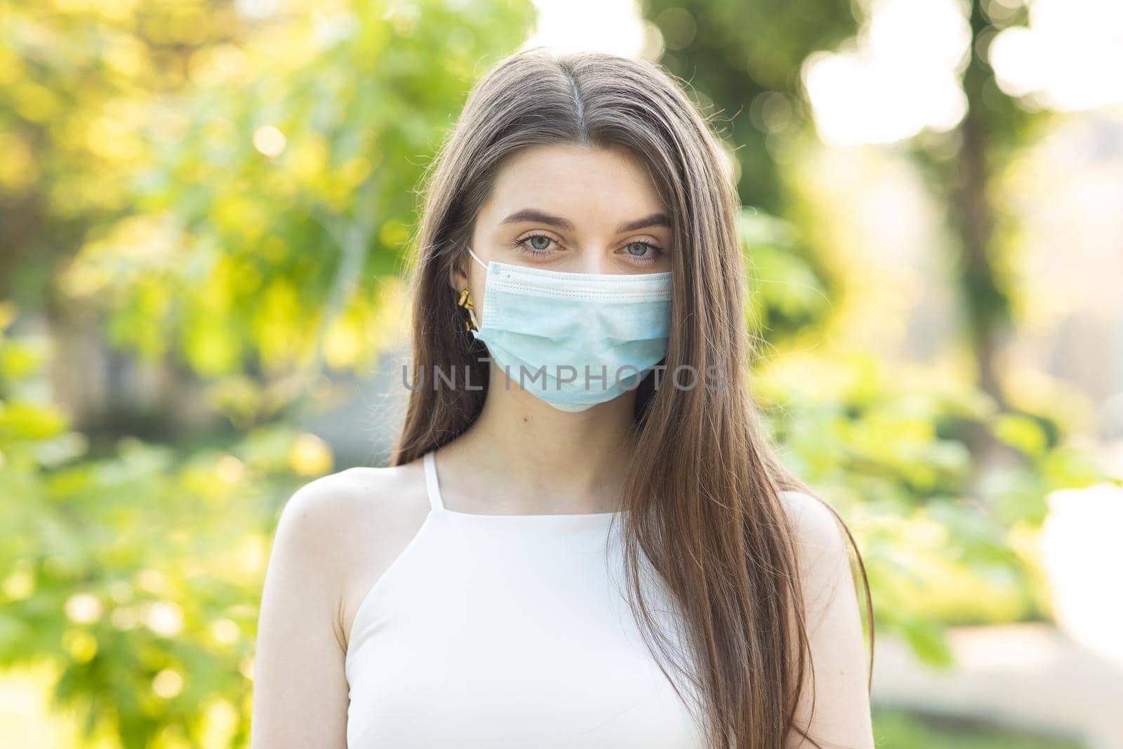 Close up portrait Young woman in medical mask. Female breathes deeply looking at camera. Isolated on park background. Health care and medical concept by uflypro