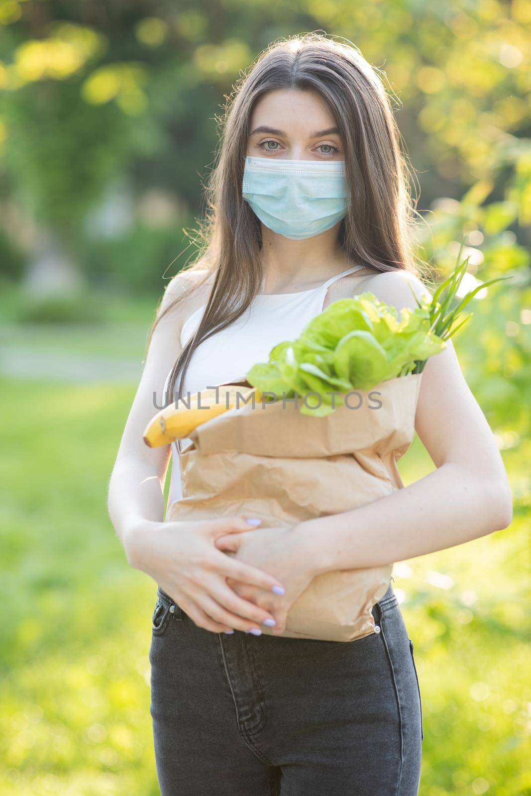 Food Delivery Young Woman in Protective Mask Carries Bag with Products From Store. Coronavirus pandemic. Delivery of food in quarantine by uflypro