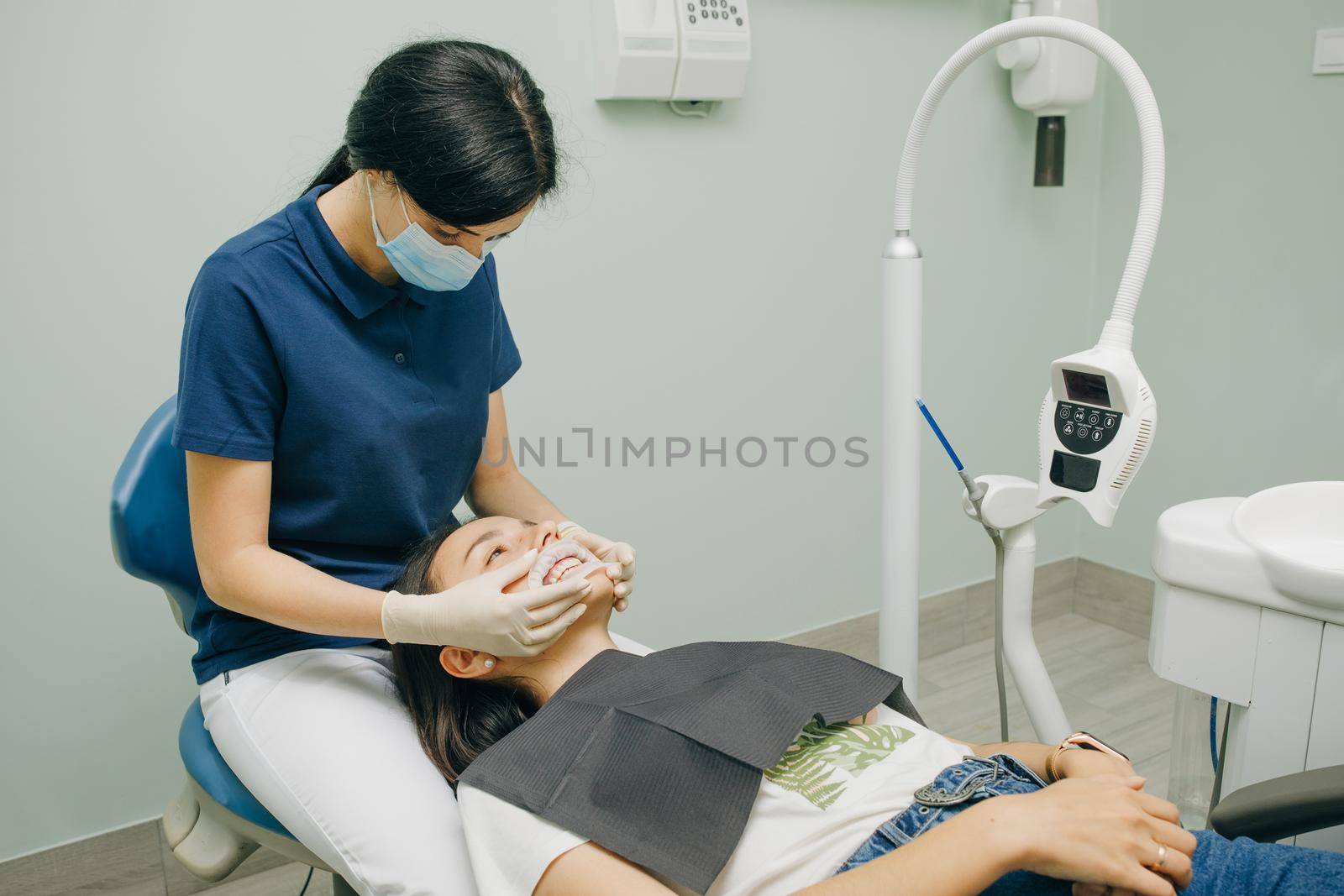Female dentist in medical white latex gloves puts rubber dam on a patient in a dental clinic. Cleaning teeth. Modern dental office by uflypro