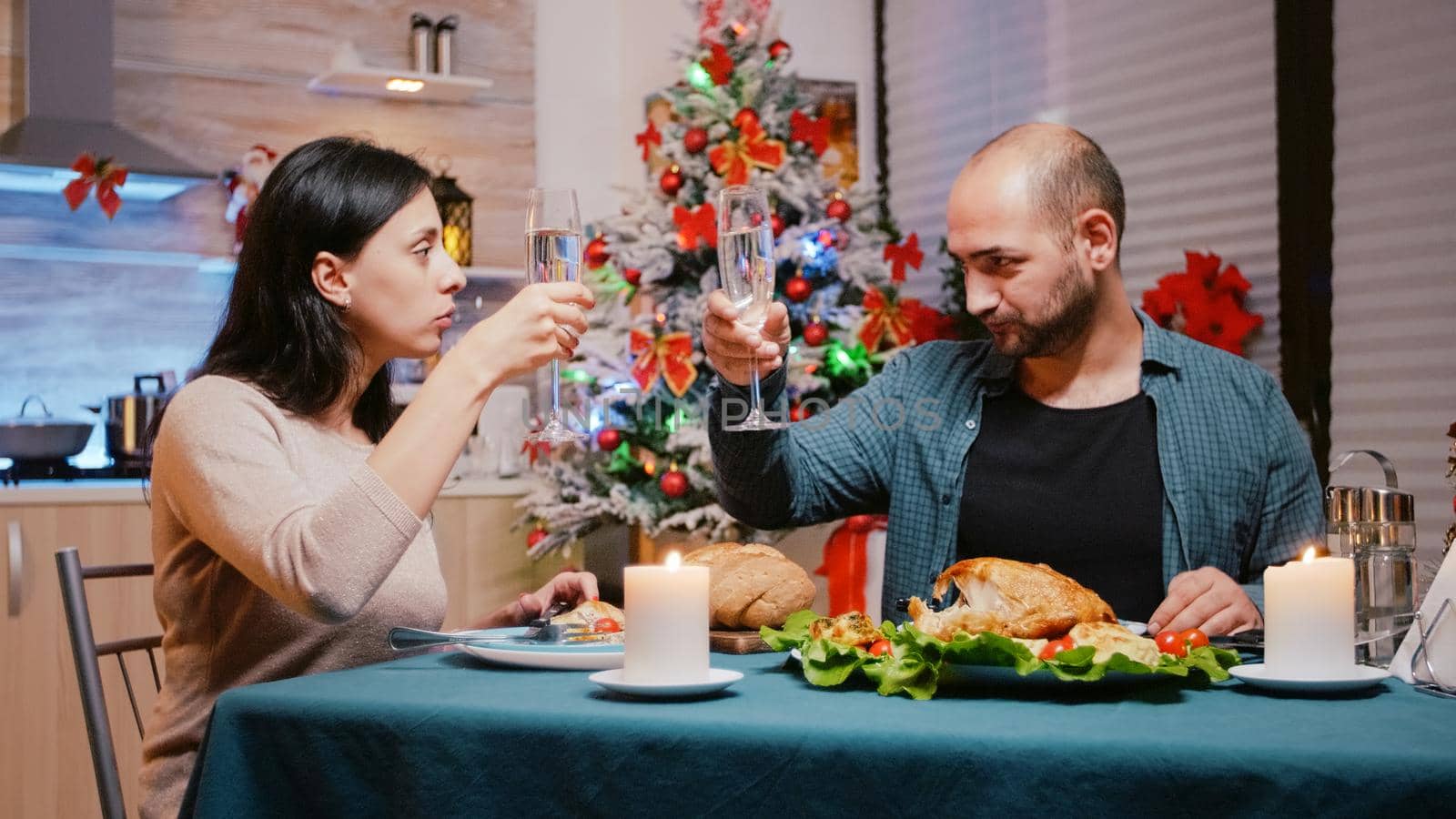 Couple clinking glasses of champagne at christmas dinner. Festive man and woman eating chicken meal and drinking alcohol for holiday celebration. People enjoying traditional festivity