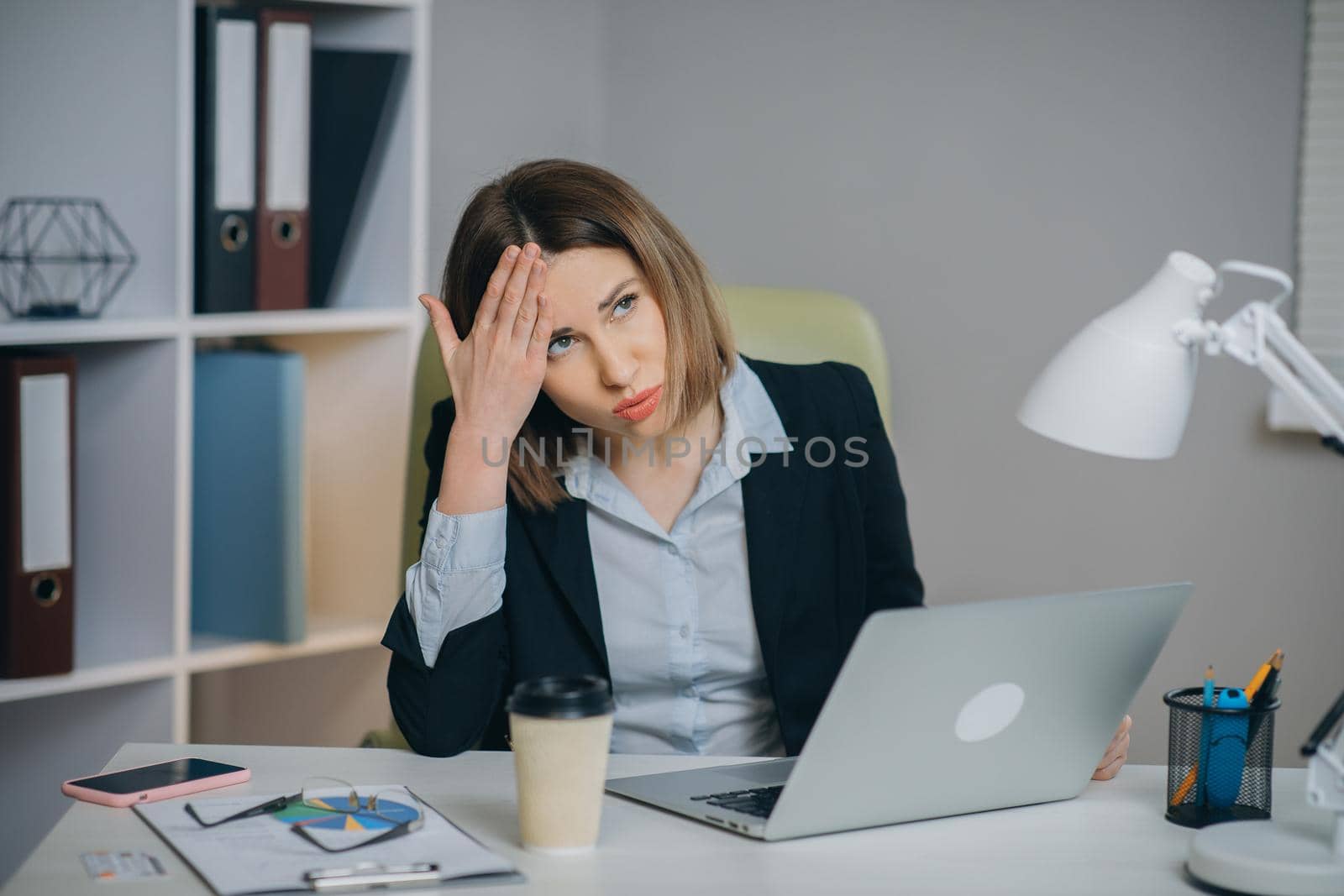 Tired woman in glasses sitting at the laptop computer while working in the office, then almost falling asleep and waking up. Indoor by uflypro