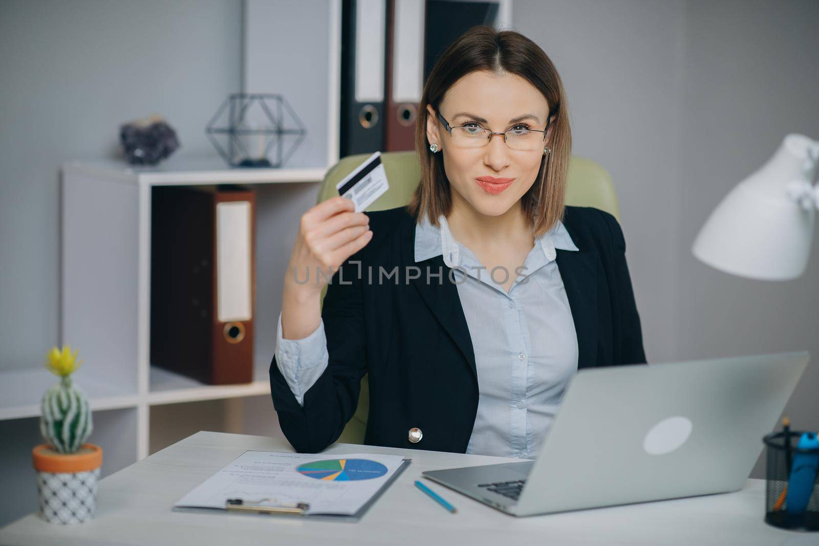 Business Woman Shopping Online with Laptop in Office. Young Woman Hold Bank Credit Card in Hand and Buying From Computer by uflypro