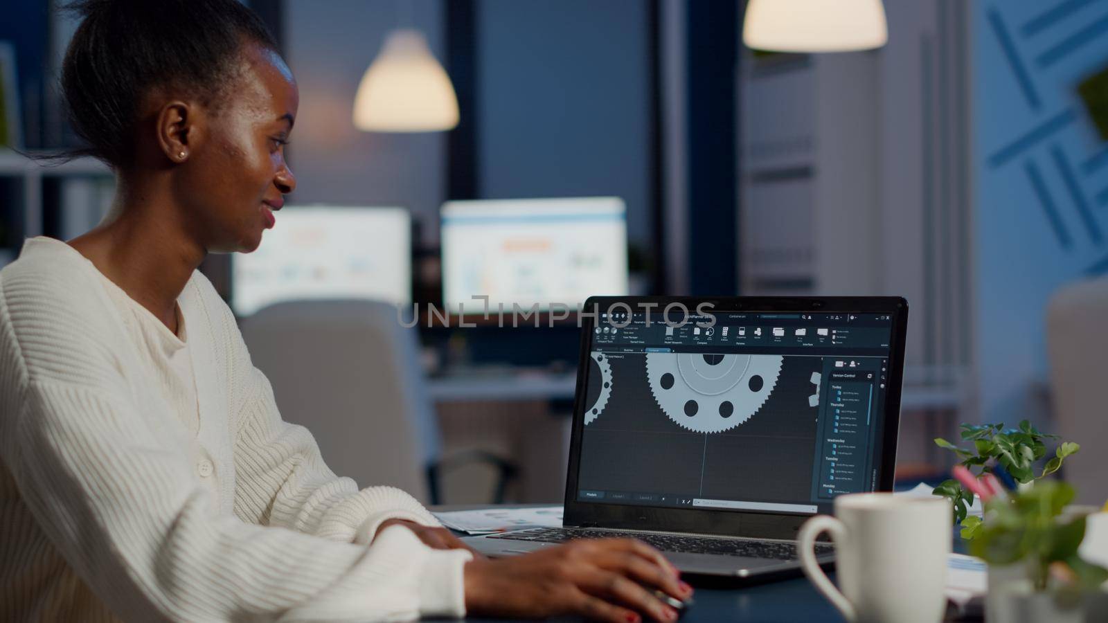 Excited black woman industry architect working on modern cad program overtime sitting in start-up office. Industrial engineer studying prototype idea on pc showing cad software on device display