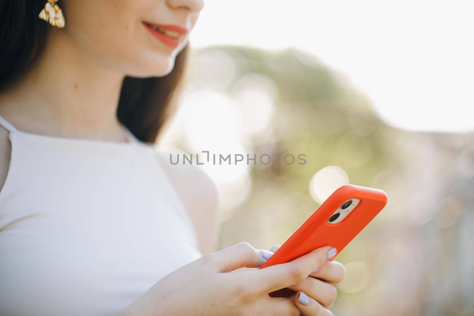 Mockup image of a woman using smart phone at outdoor and green nature background. Girl Hands holding smartphone. Woman Using Smartphone in Beautiful Green Park. Technology outdoors.