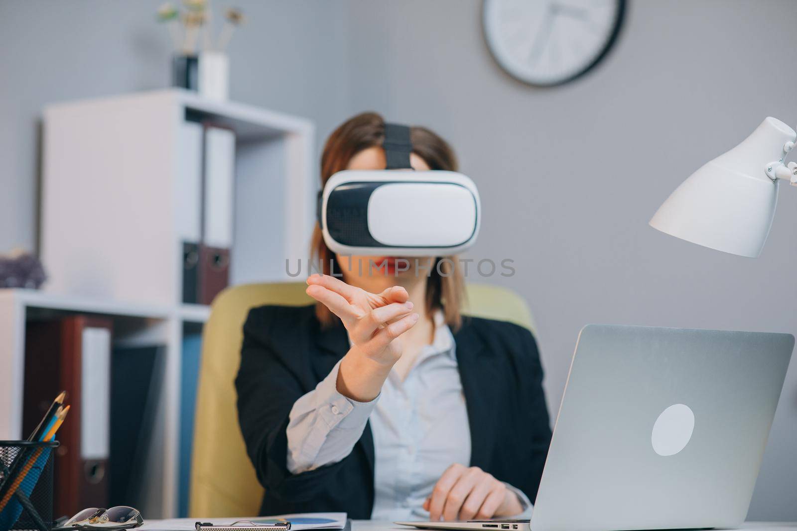 Modern business woman wearing virtual reality glasses in office. Young girl using VR goggles in office. Pretty woman working in augmented reality at workplace.