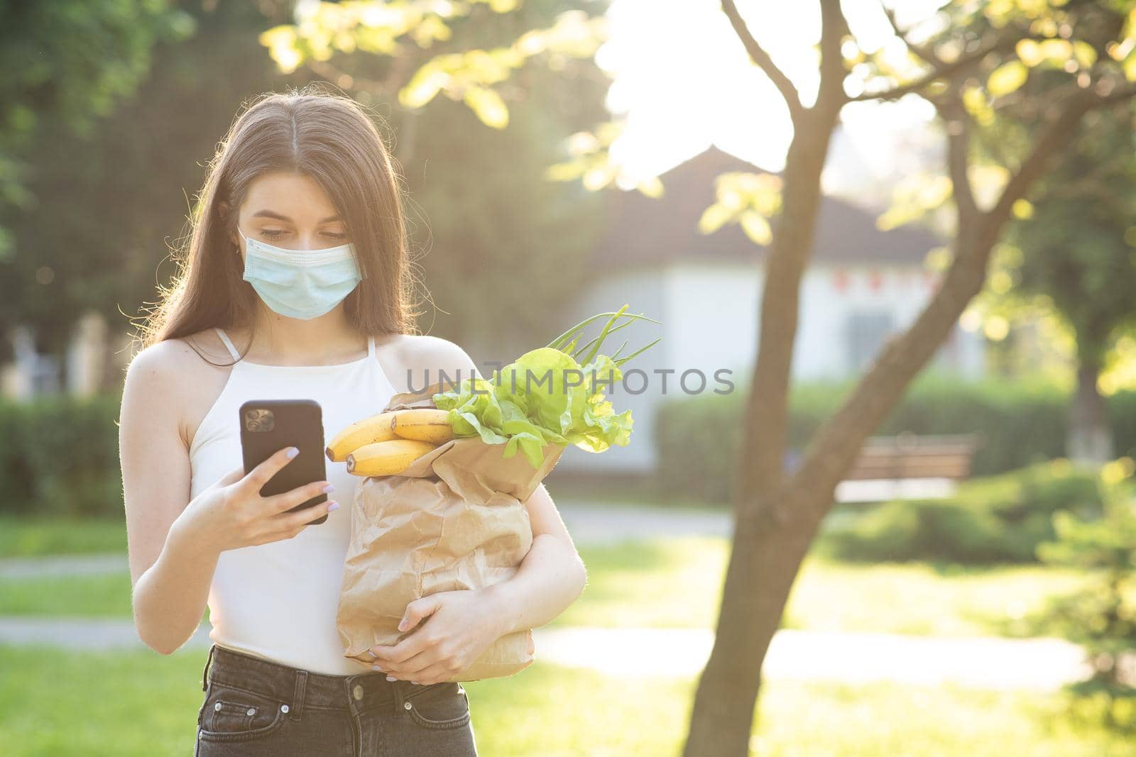 Caucasian young pretty woman in medical mask walking the street carrying packet with fresh food. Female beautiful going to deliver grocery.
