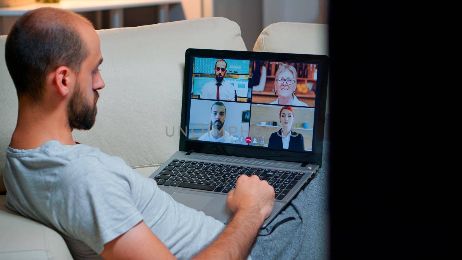 Over shoulder view of man in pajamas having online conversation with teammates by DCStudio